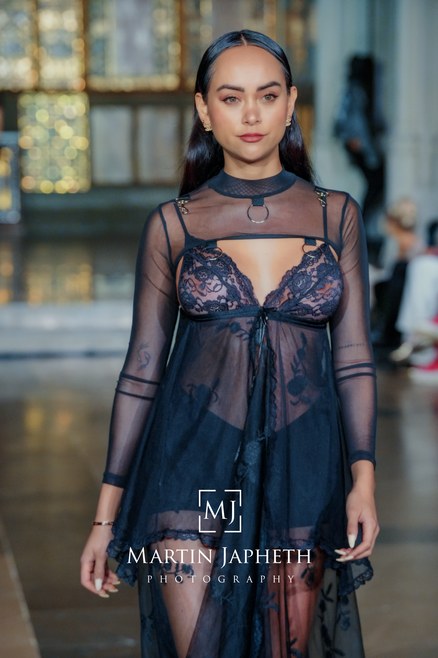 Fashion model wearing sheer black mesh top with navy lingerie on runway at fashion show.