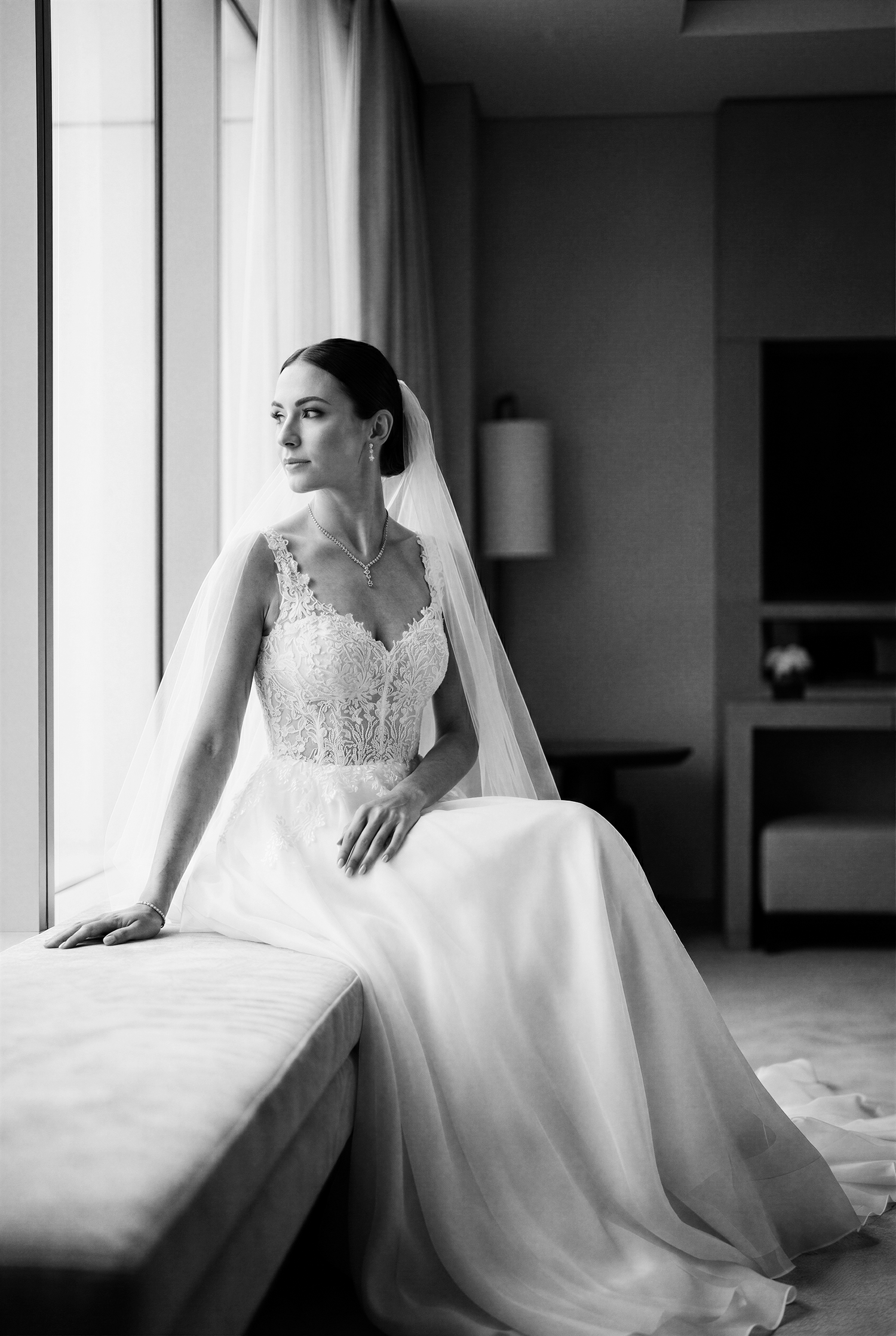 A black and white collage of a bride in an elegant lace wedding gown sitting by a window in soft natural light.