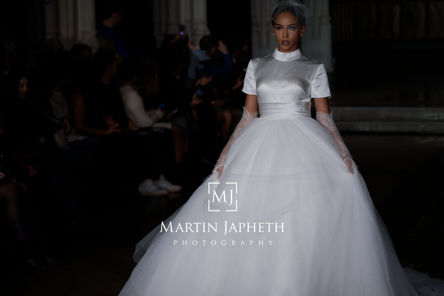 A bride in a flowing white ball gown wedding dress stands elegantly in front of a dark background.
