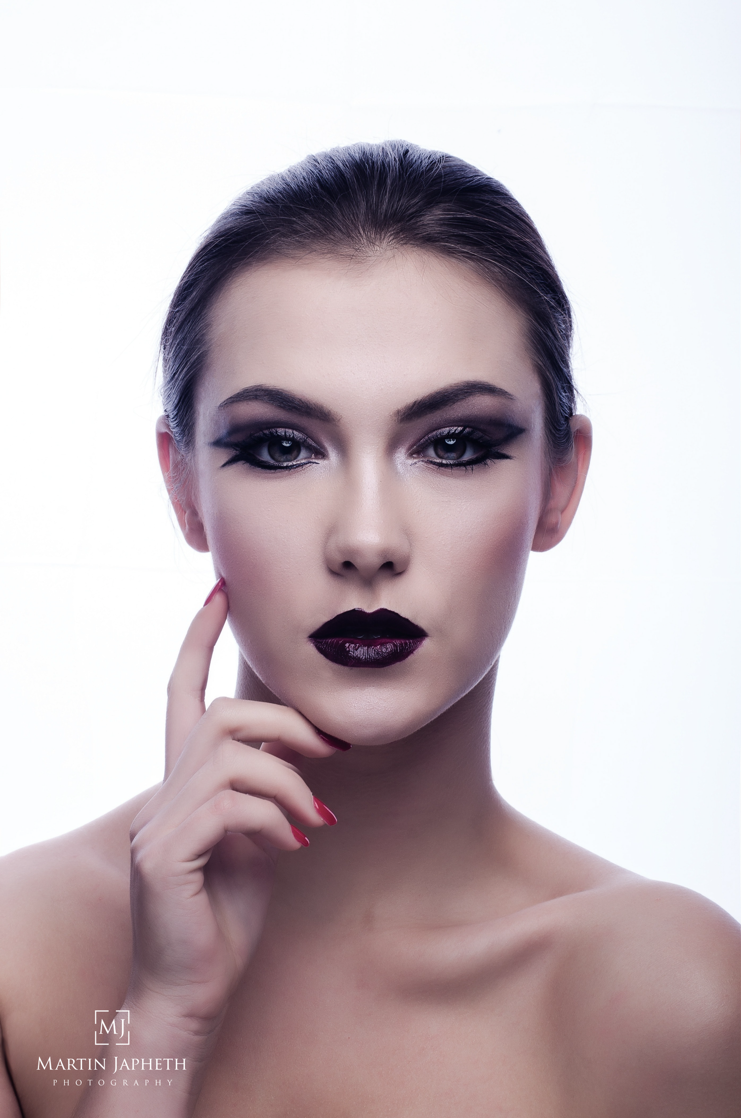 Close-up beauty portrait of a woman with dramatic dark makeup and bold dark lips on white background.