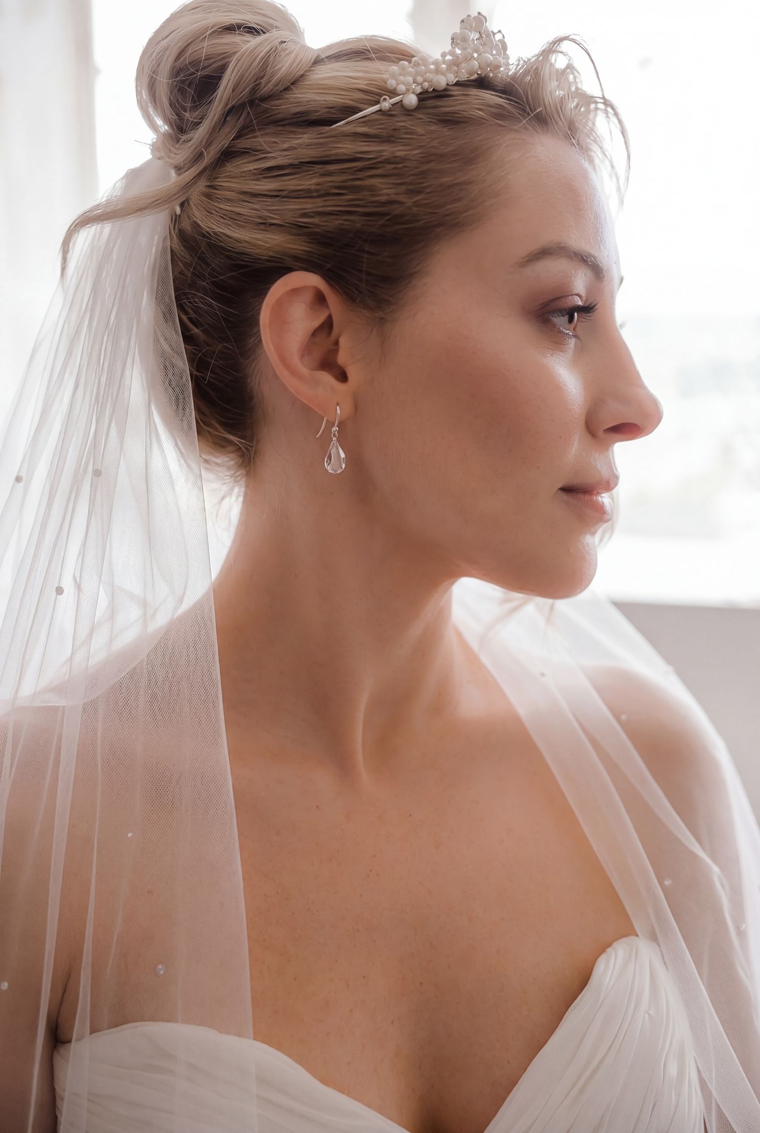 Bride in profile wearing crystal drop earrings, floral tiara, and sheer veil with elegant updo hairstyle. Chateau Rhianfa Wedding