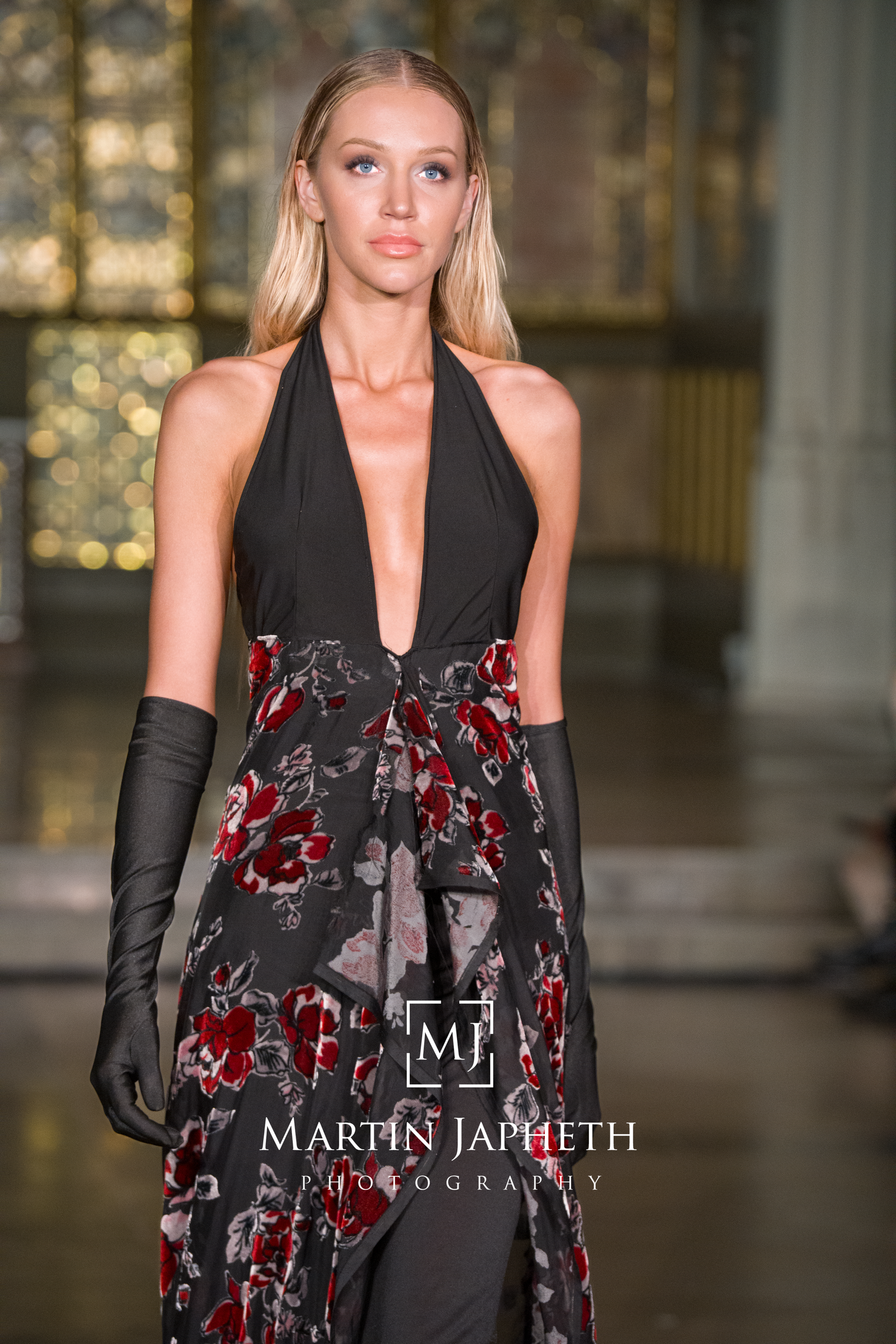 Fashion model wearing elegant black and red floral evening ensemble with long gloves on runway.
