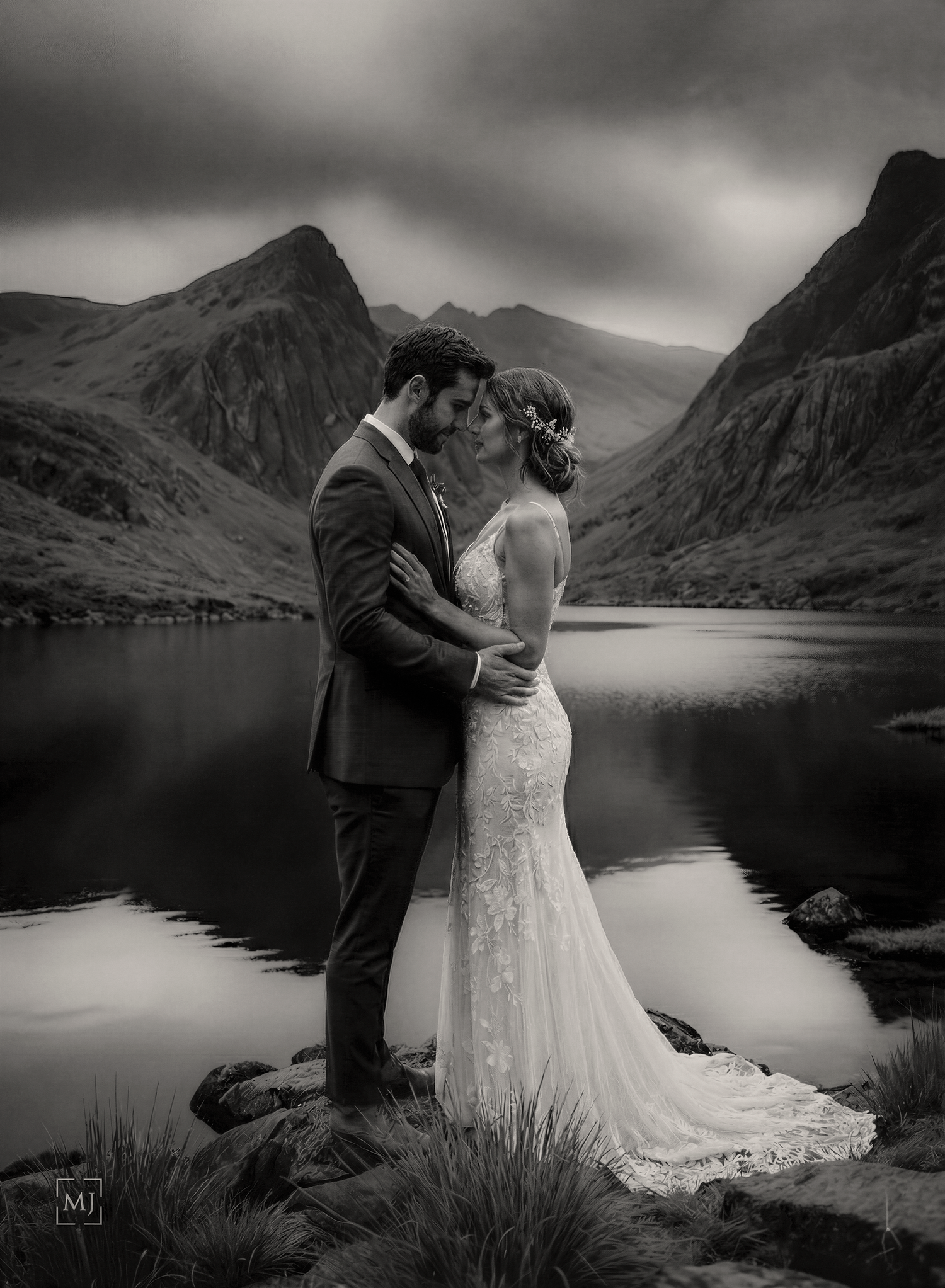 A romantic black and white wedding photoshoot by a serene Ogwen lake with dramatic cloudy skies in the background.