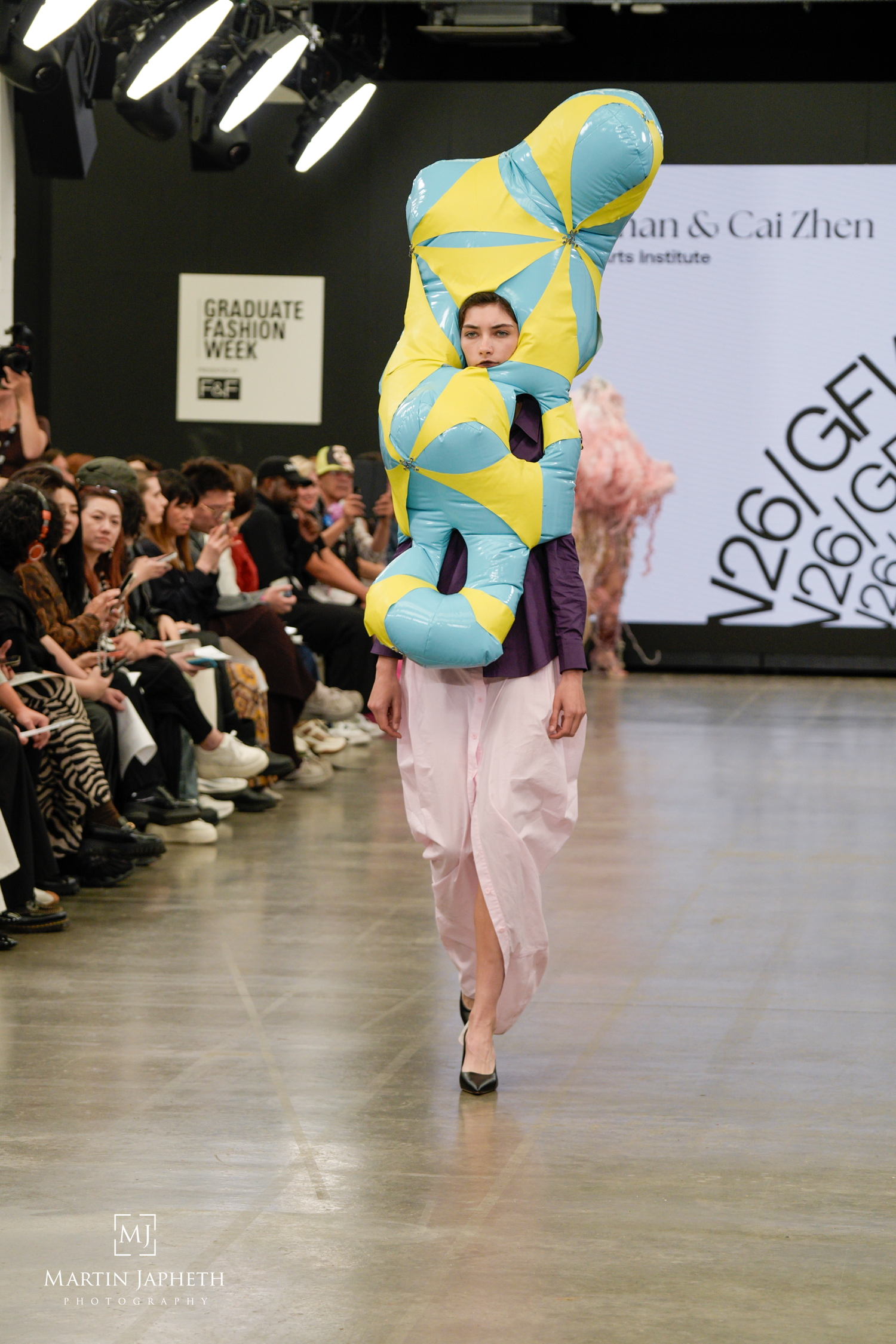 Model walks runway at Graduate Fashion Week wearing a bold sculptural turquoise and yellow inflatable top with a pink skirt. Martin Japheth