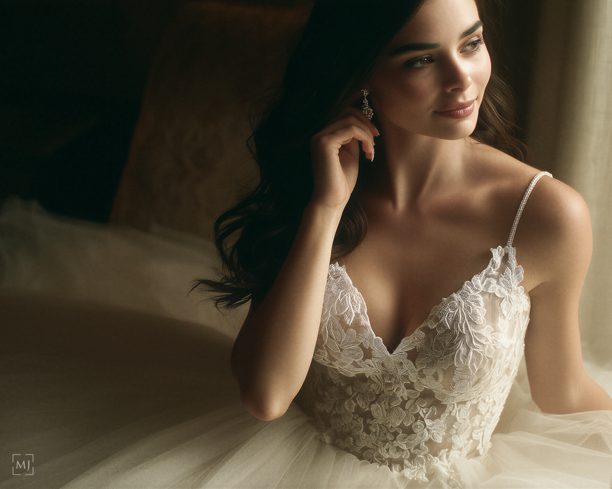 A bride in an elegant white lace wedding dress poses in soft natural light for a romantic bridal portrait series.