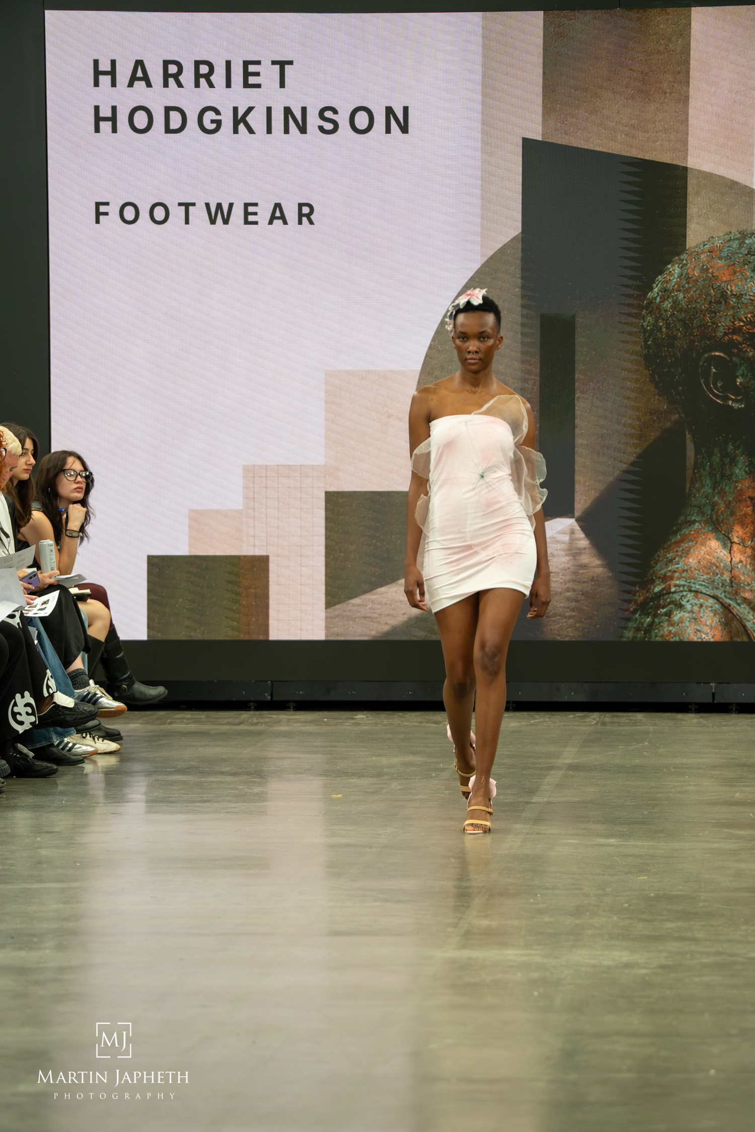 Model walks runway in white mini dress at Harriet Hodgkinson Footwear fashion show, photographed by Martin Japheth.