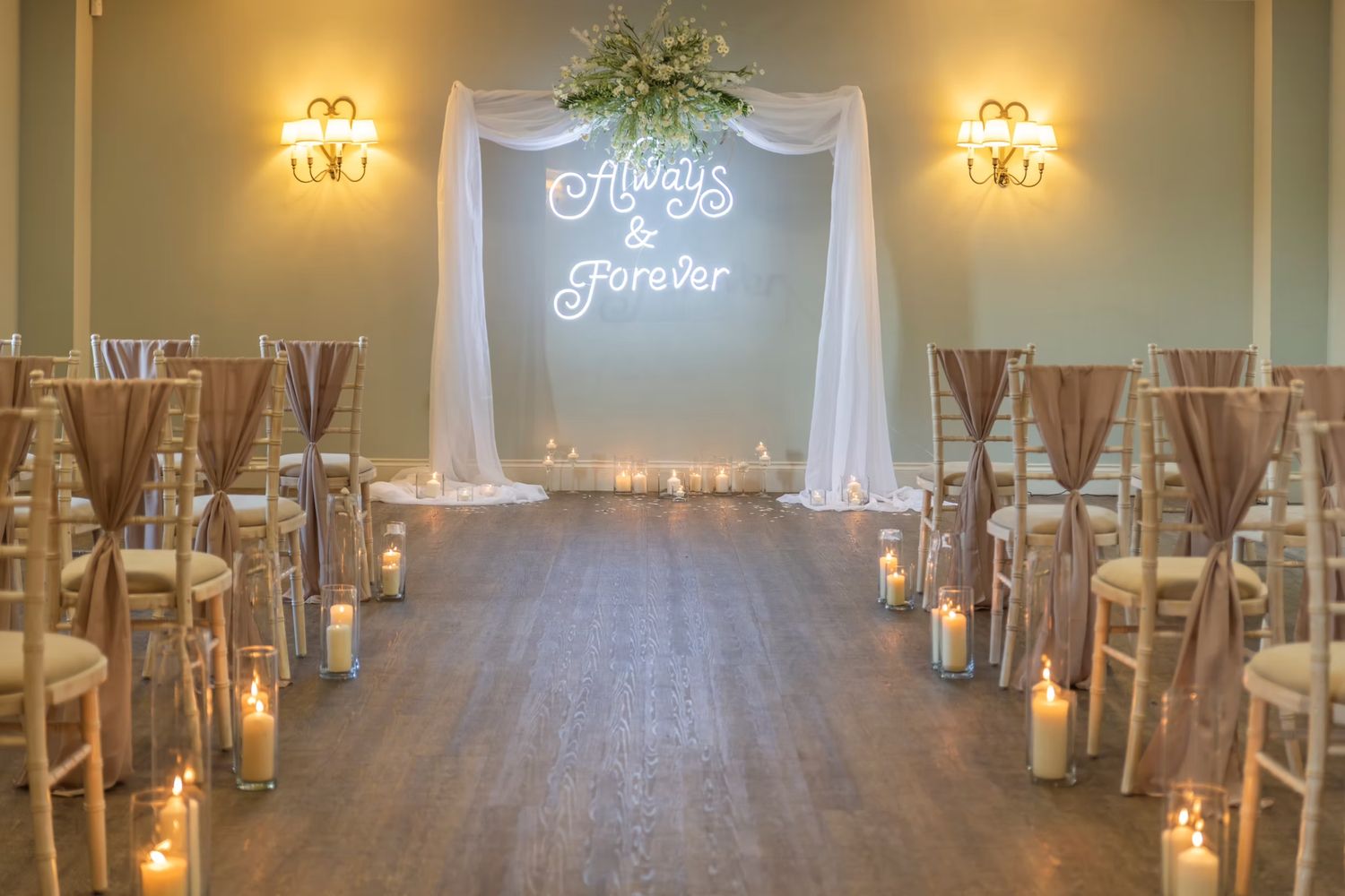 An elegant wedding reception venue with white chairs, warm lighting, and crystal chandeliers creating a romantic atmosphere. Hayloft at Bodn