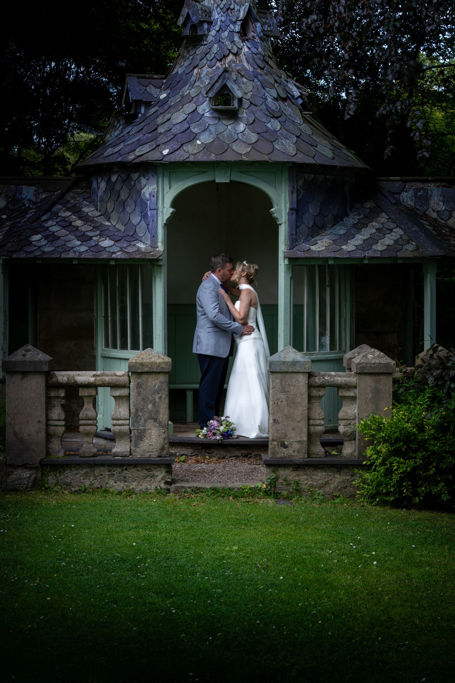 Bride and groom share a romantic kiss in a charming garden pavilion surrounded by lush greenery on their wedding day. at Chateau Rhianfa