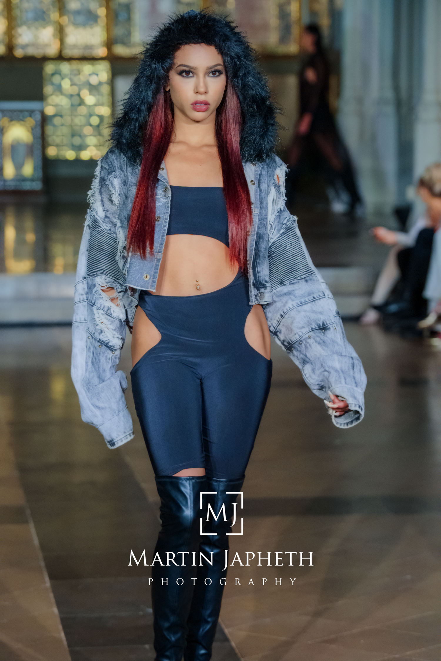 Fashion model walks runway in black cutout bodysuit paired with distressed light blue denim jacket during fashion show.