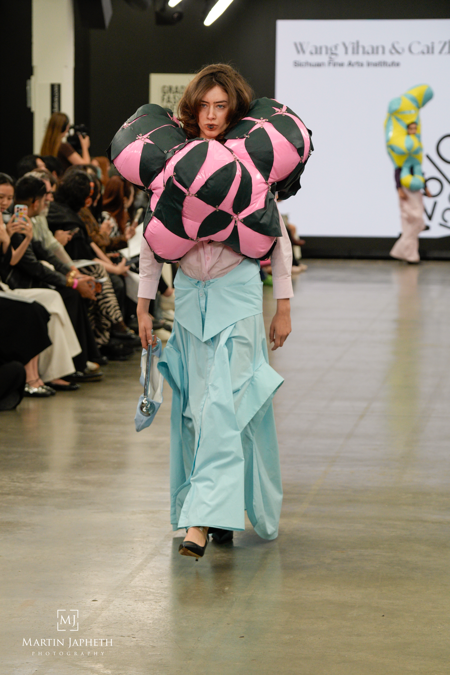 Model walks runway in avant-garde pink and black sculptural top with flowing mint skirt at Wang Yihan fashion show. Martin Japheth