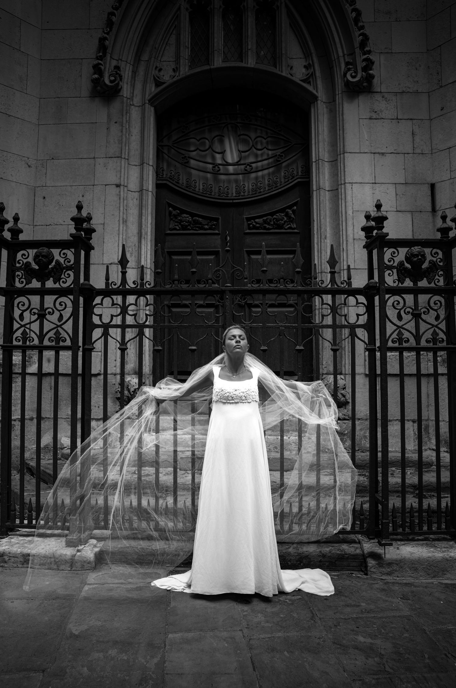 Bride spreading her veil wide before the iron gates of St Dunstan in the East, black and white London portrait