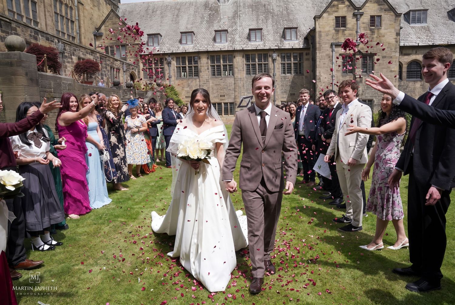 Bride and groom walk through confetti shower at outdoor wedding ceremony at hBangor University with Martin Japheth Photography.