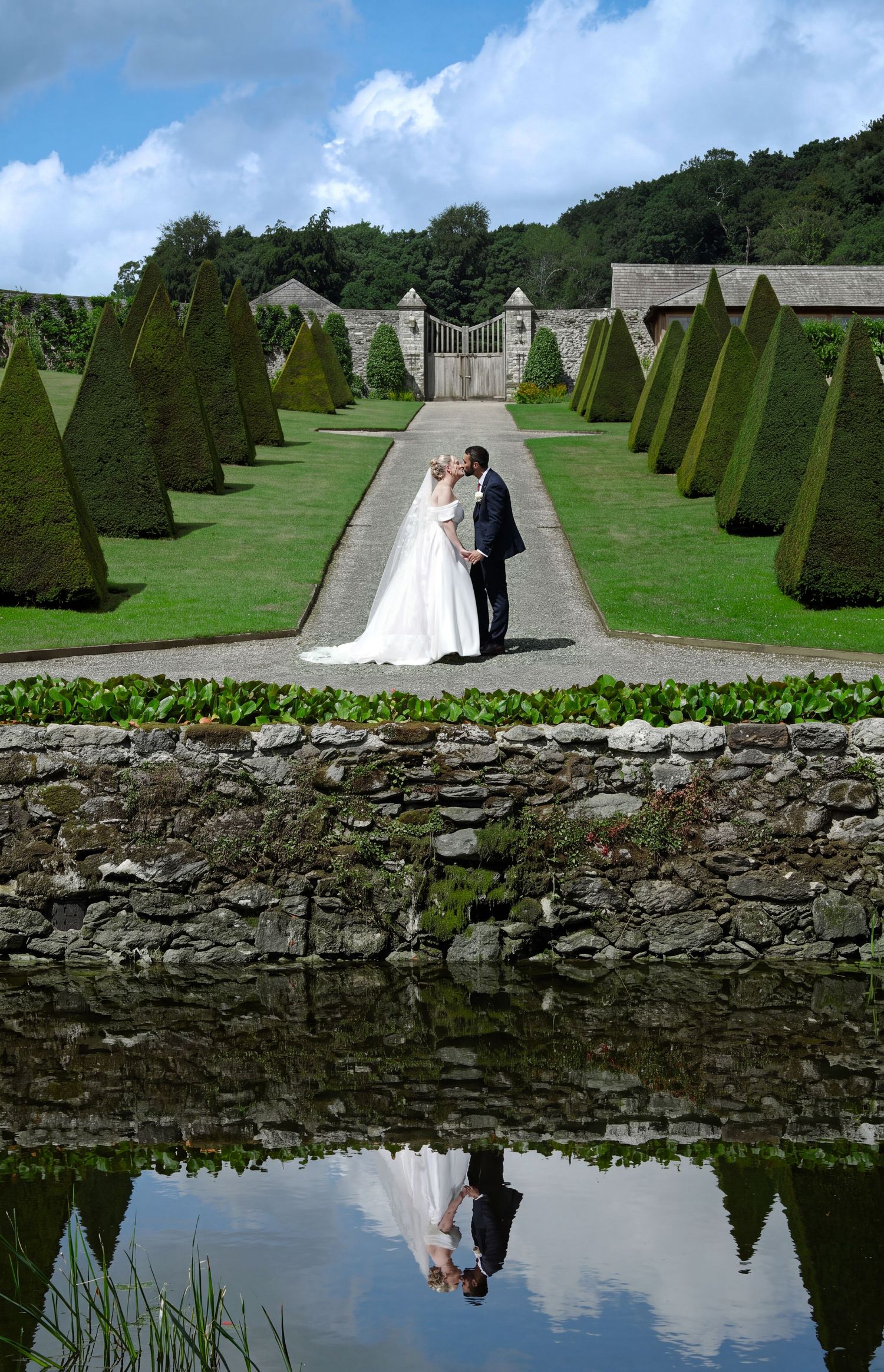 Bride and groom beside the river and waterfall in the valley garden at Plas Cadnant, Anglesey