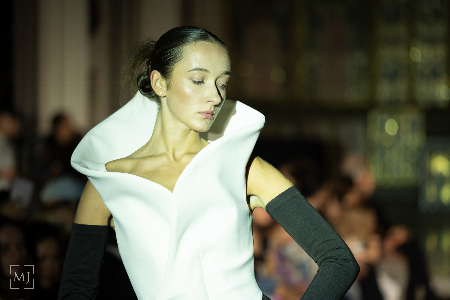 Models present crisp white collared garments against a dark backdrop during a runway show.