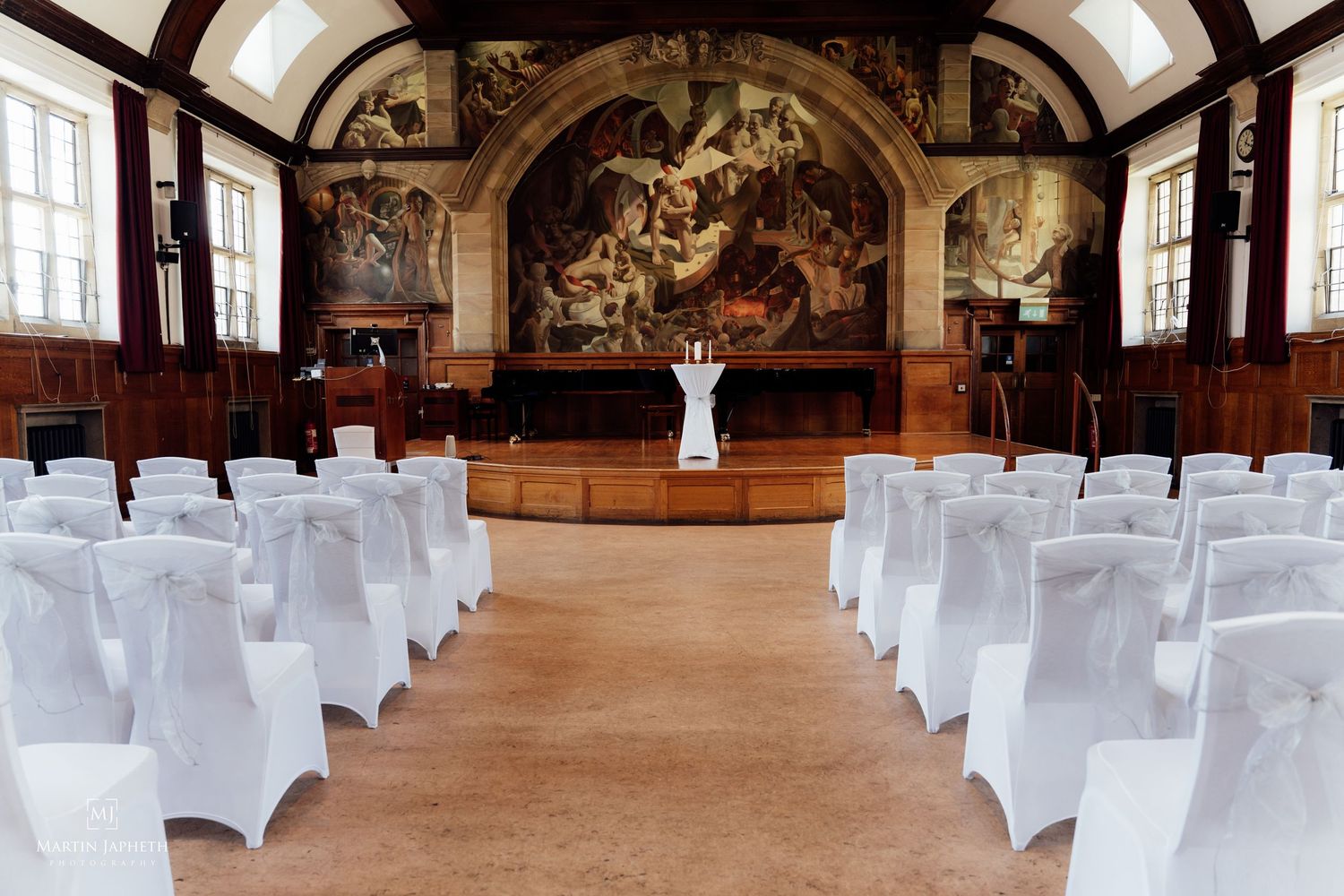 Elegant wedding at Powis hall at Bangor University with white chair covers, ornate murals, and a floral centrepiece on a marble floor.