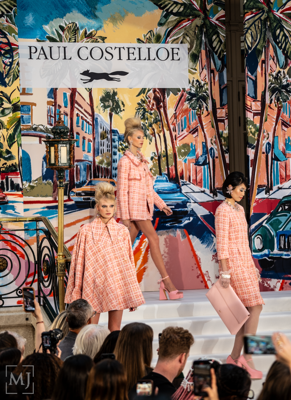 Fashion models showcase pink checkered outfits on a runway with vibrant urban mural backdrop at Paul Costelloe show.