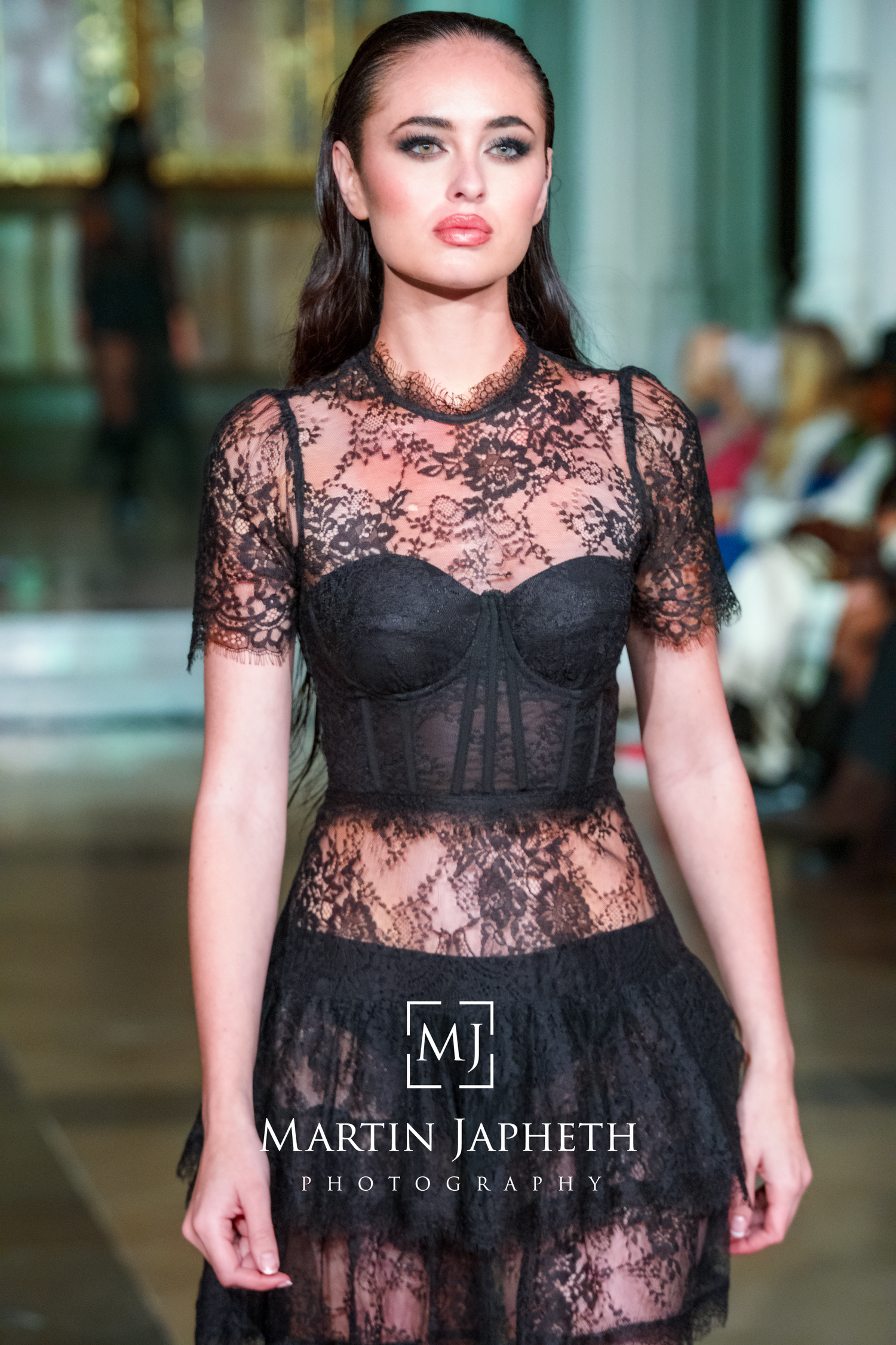 Fashion model walks runway in black lace sheer dress at fashion show event.