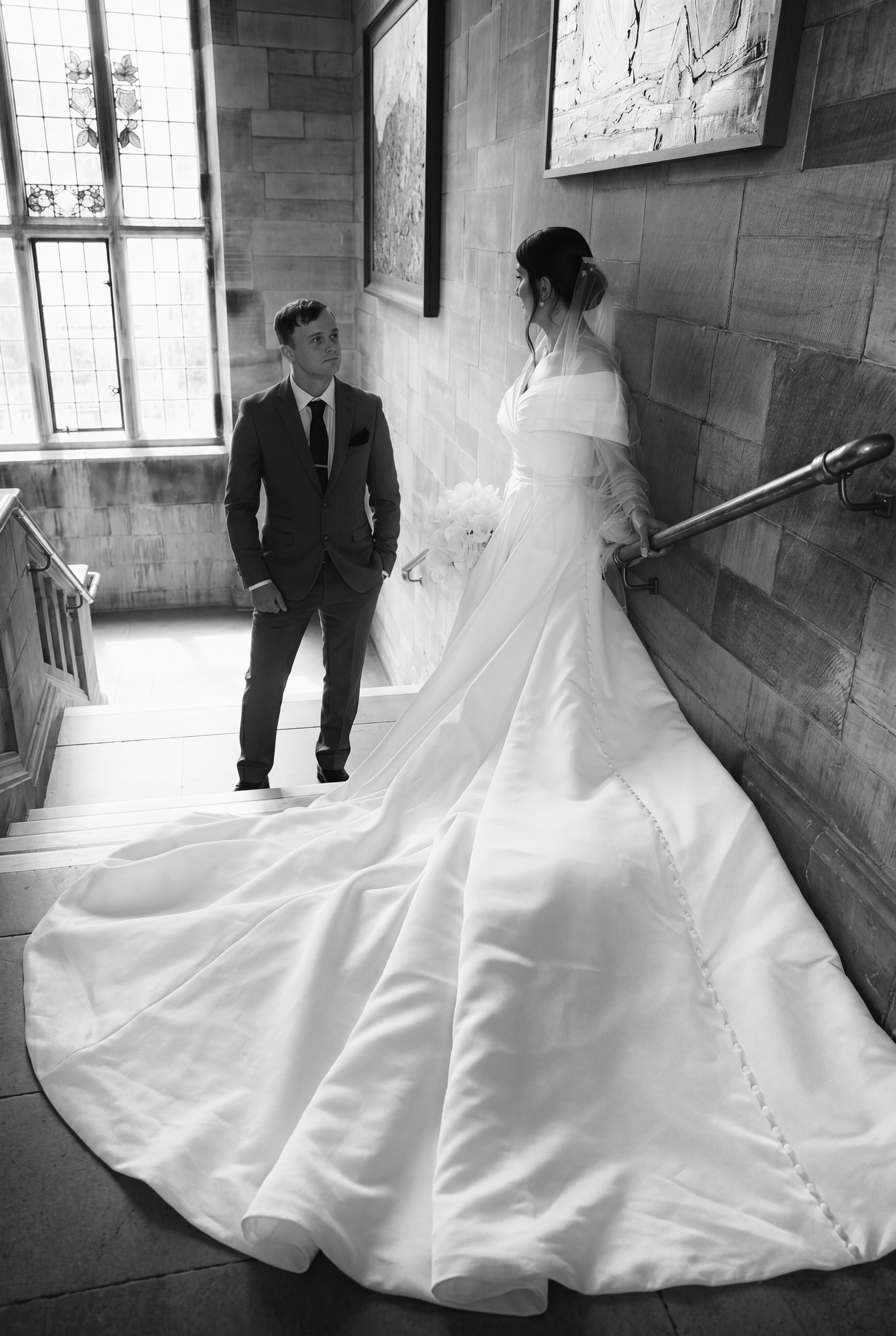 Black and white wedding photo of bride in elegant gown with long train and groom in suit on grand staircase at Bangor University Wedding.