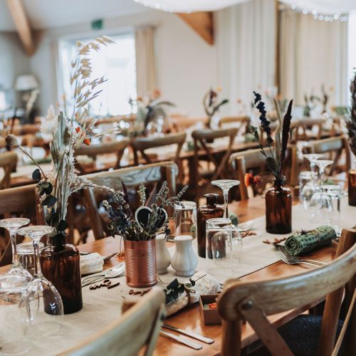 Rustic wedding reception tables with dried floral centerpieces in amber bottles, wooden cross-back chairs. Nant Gwrtheyrn