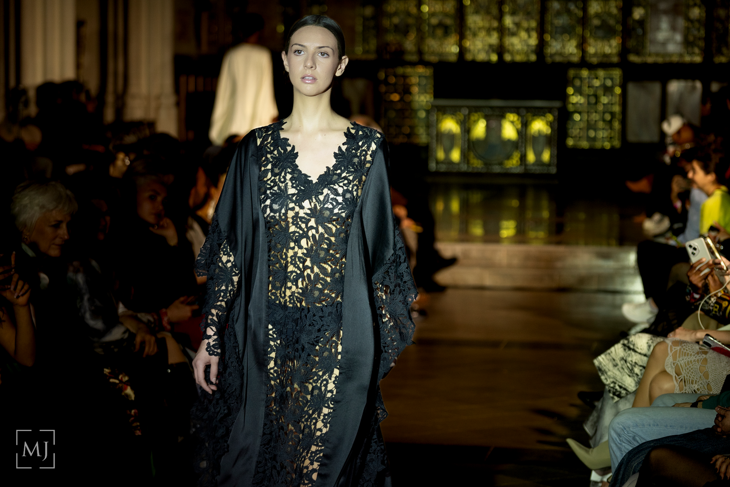 Models walk the runway in elegant black evening gowns with gold embellishments during a fashion show.