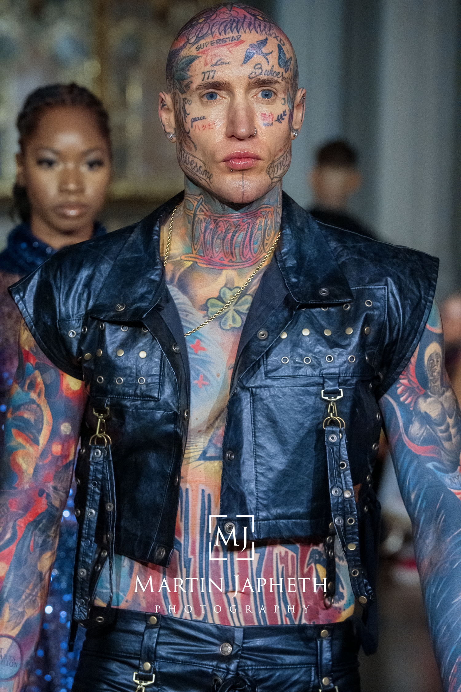 Fashion runway show featuring black leather motorcycle vests with edgy punk styling and tattoo-inspired designs.