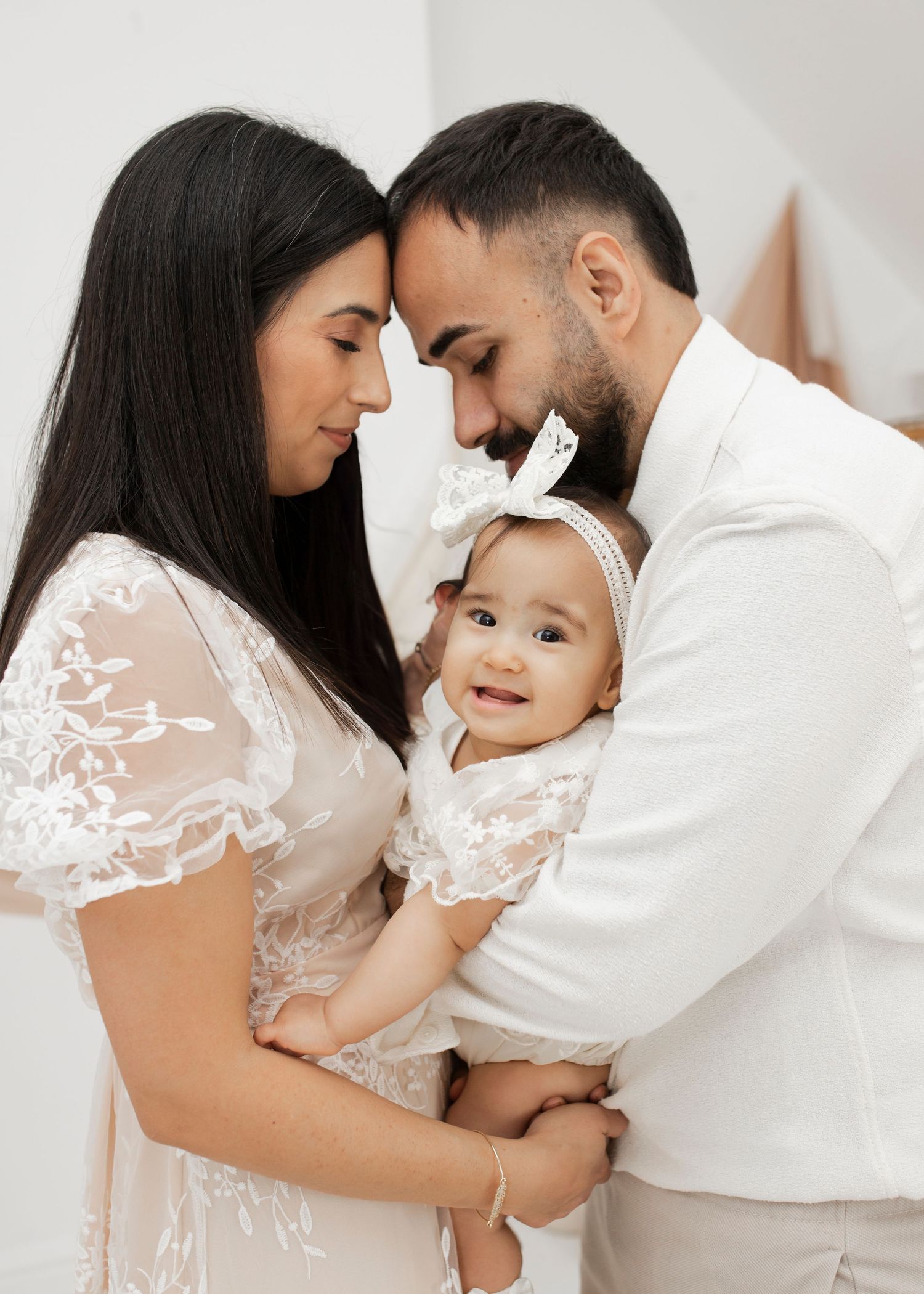 Family portrait in white outfits sharing tender moment together.