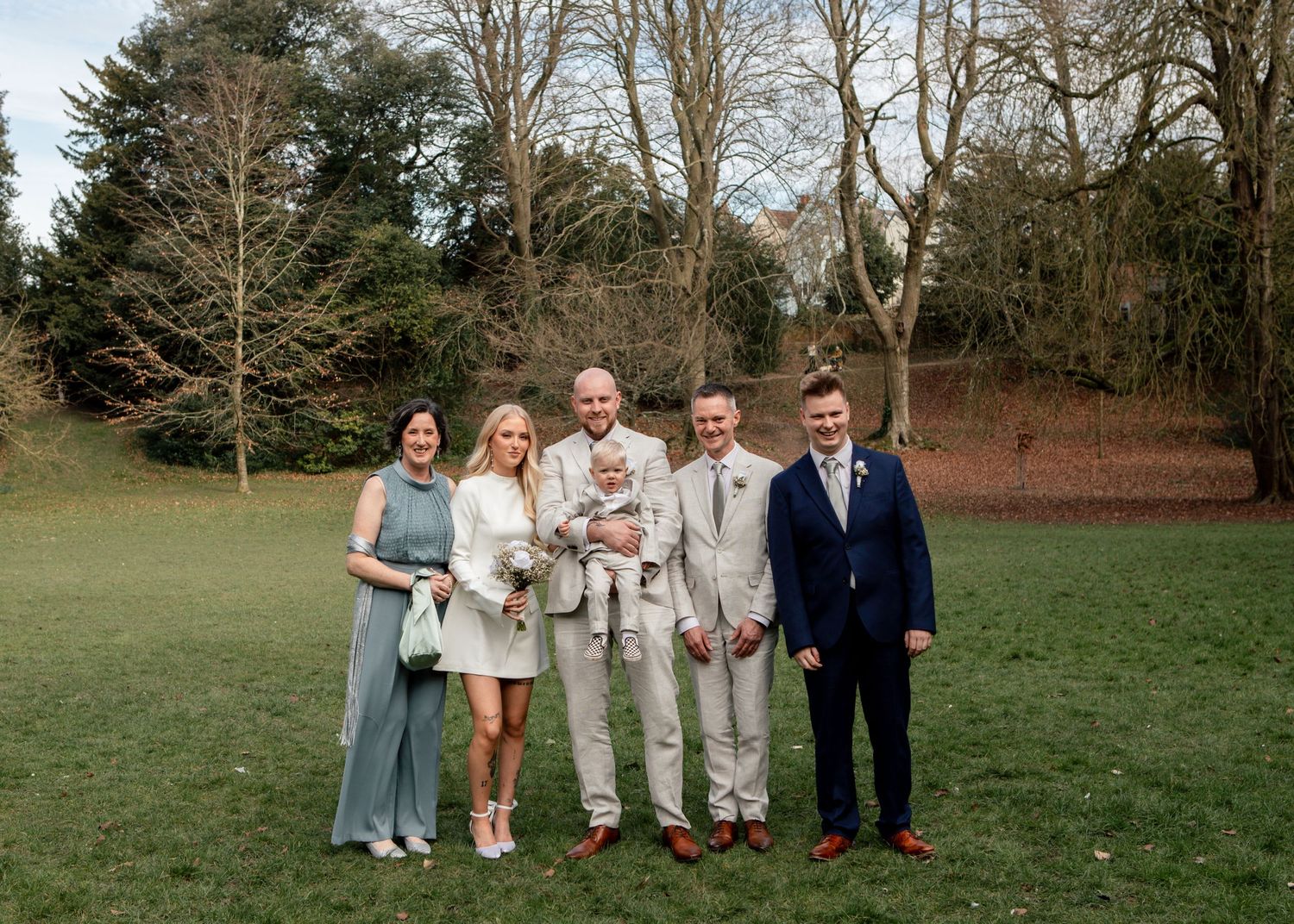 Family group portrait outdoors with trees in background.
