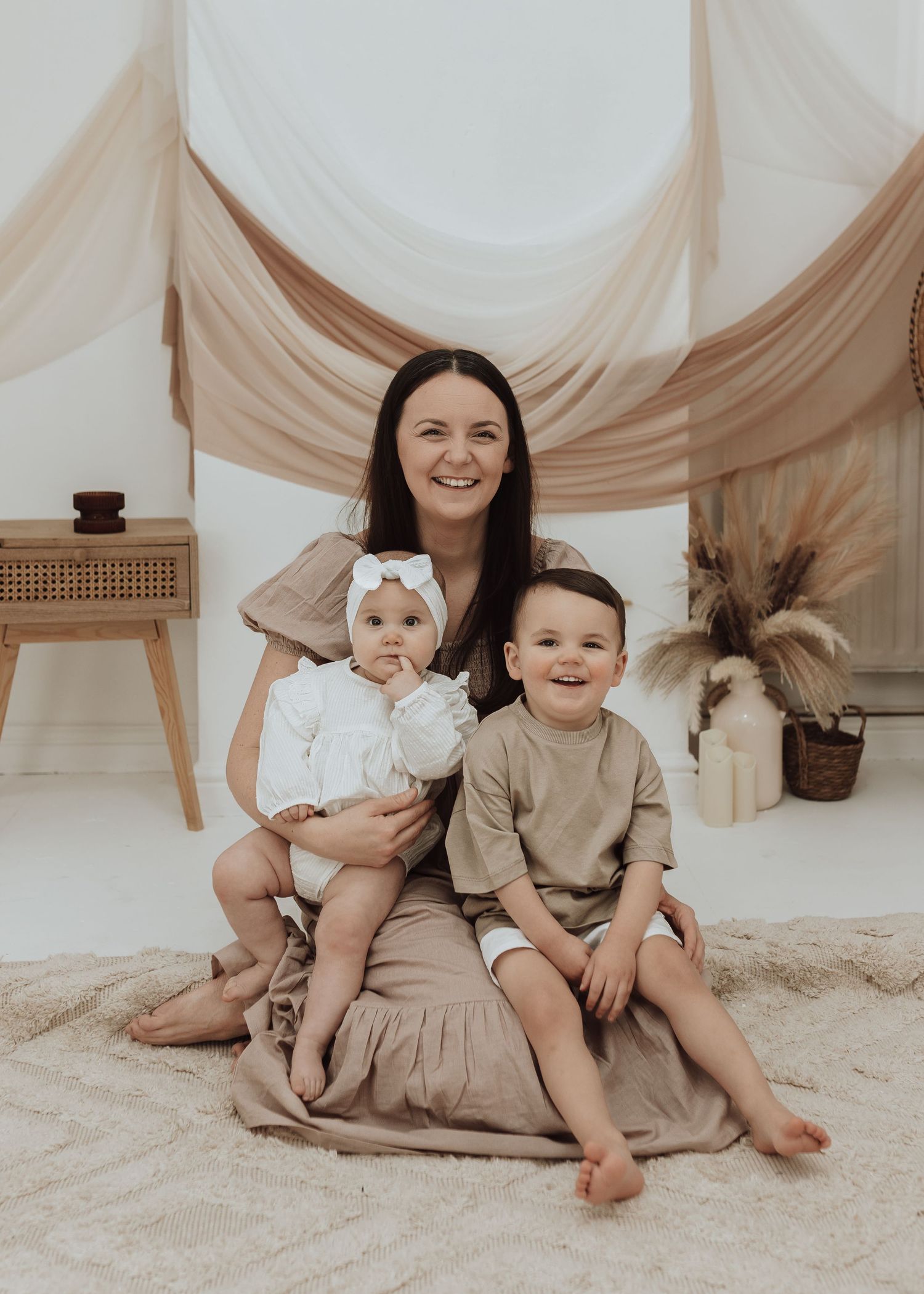 Studio family session with neutral earth tone outfits on cream carpet with fabric backdrop.