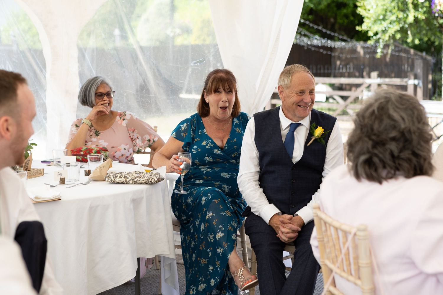 Wedding reception under white tent with guests seated at decorated tables.