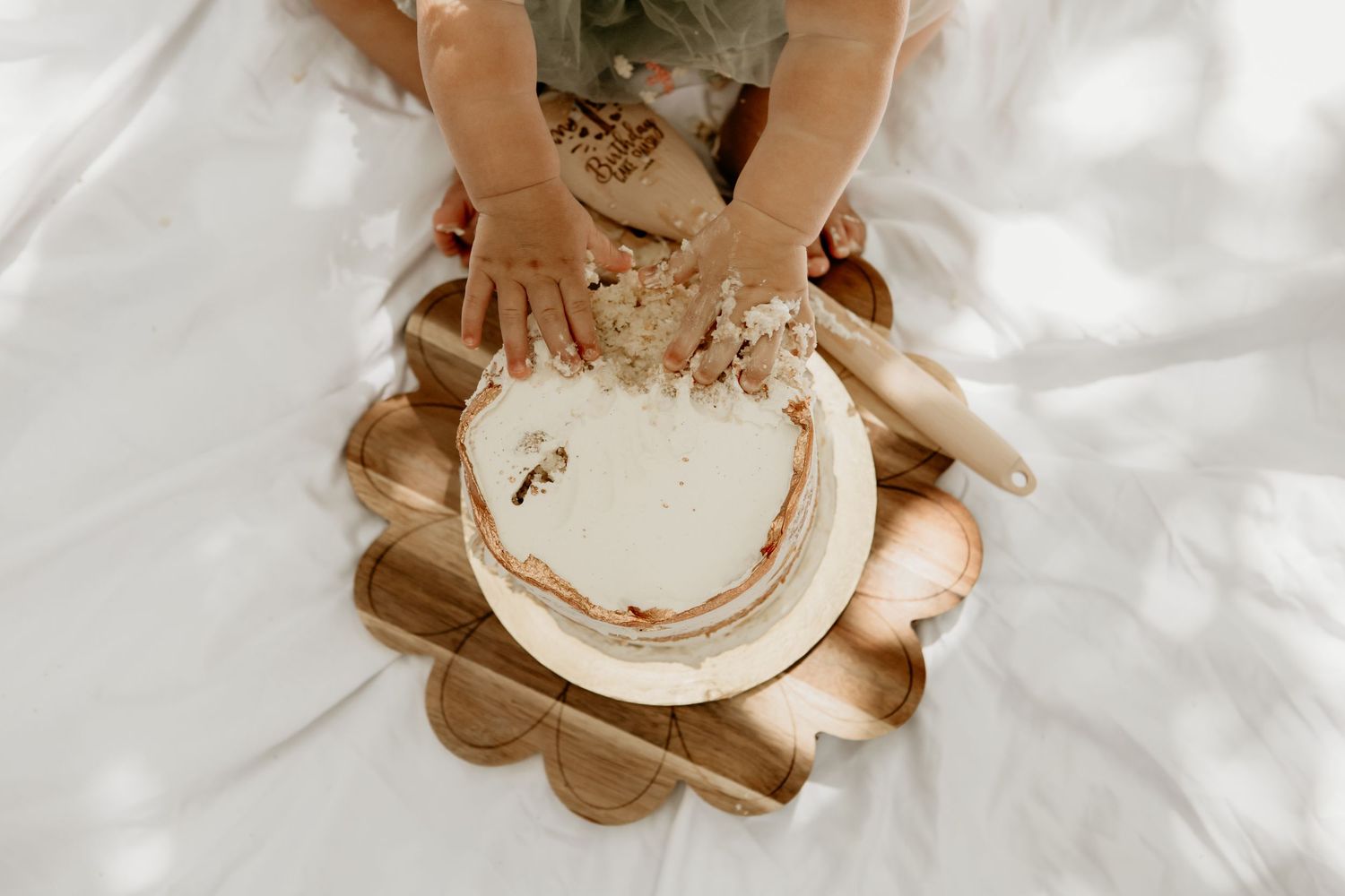Overhead view of white cake smash setup on blanket with wooden decorative elements.