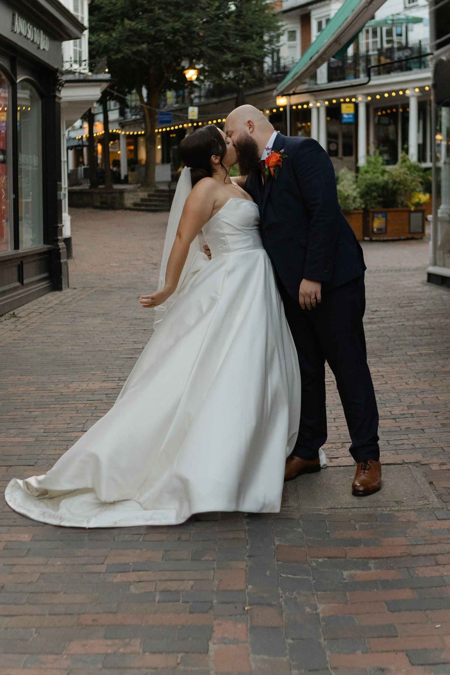 Wedding couple walking on cobblestone street with shops in background.