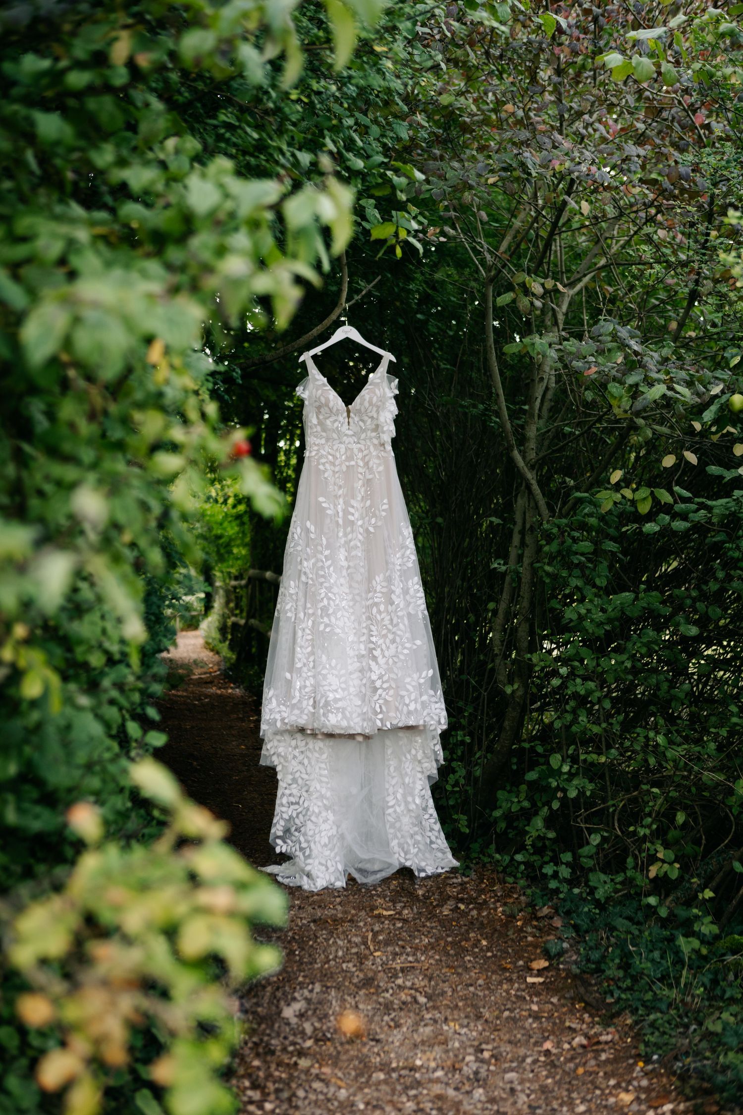 Delicate lace wedding dress hanging in a lush garden setting.
