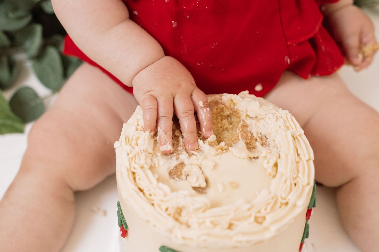 Cake smash session showing messy cream frosting and tiny hands.