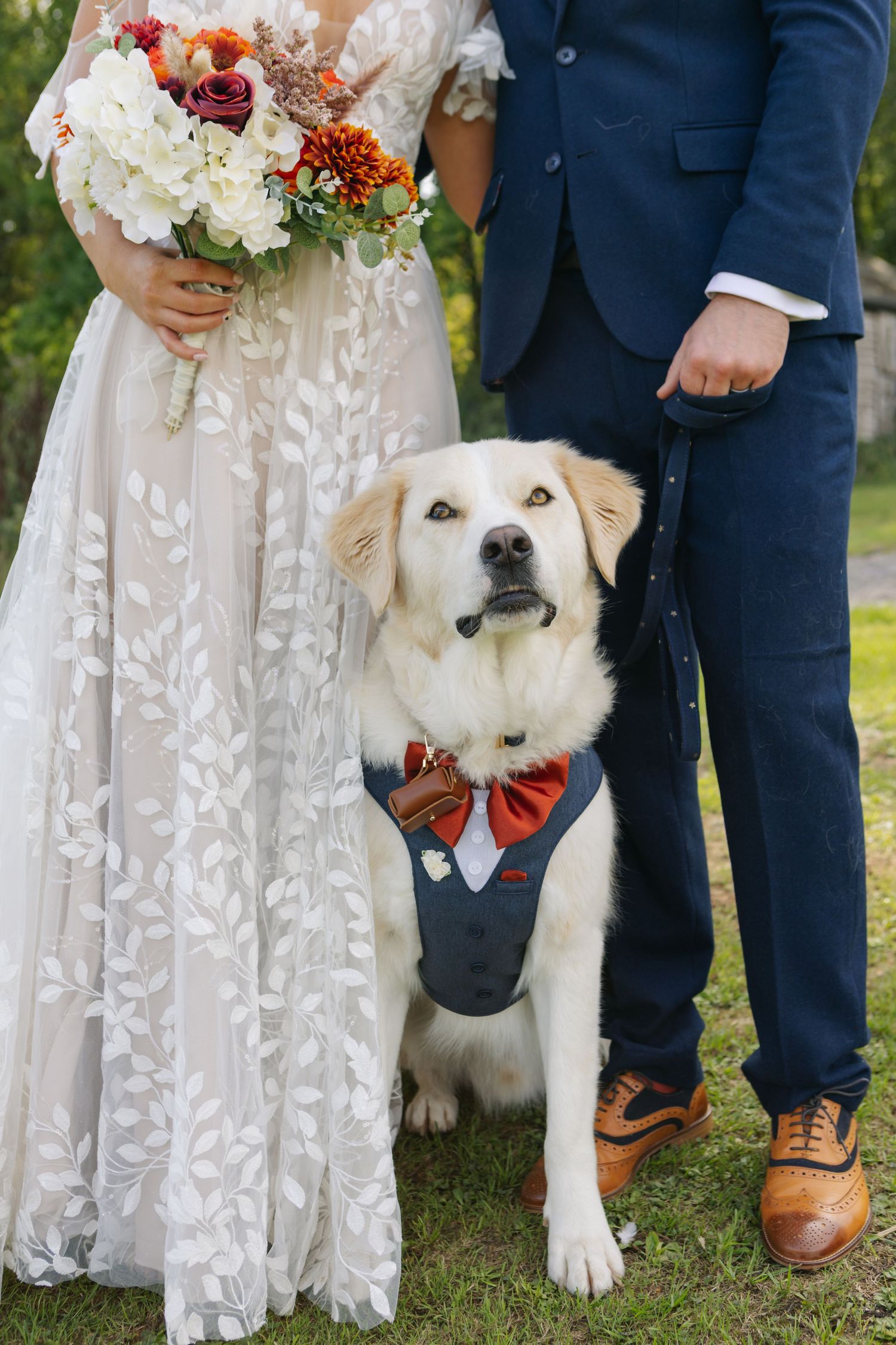 Wedding party poses with adorable white dog wearing formal bowtie attire.