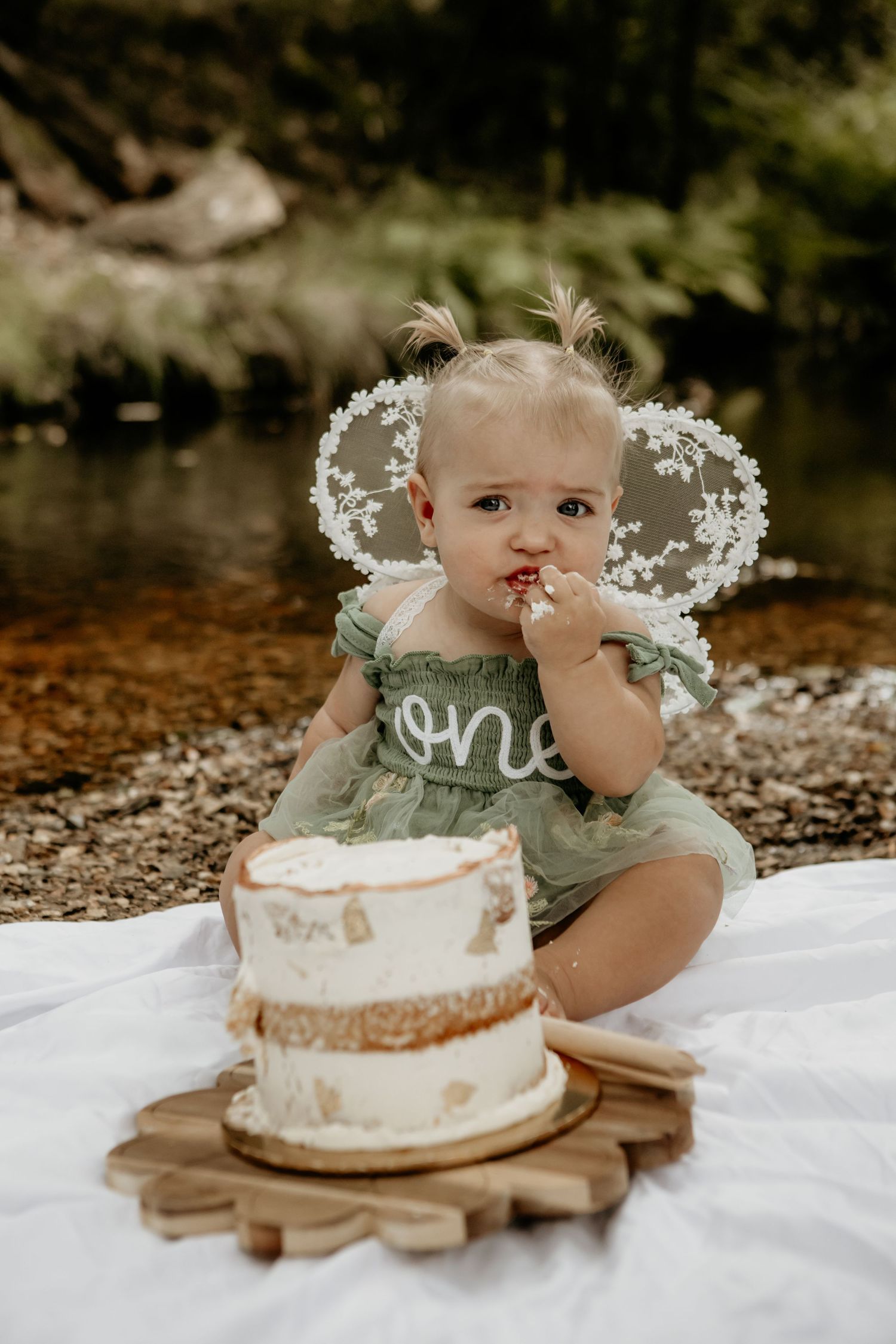 Cake smash photography session featuring white cake on wooden platter outdoors.