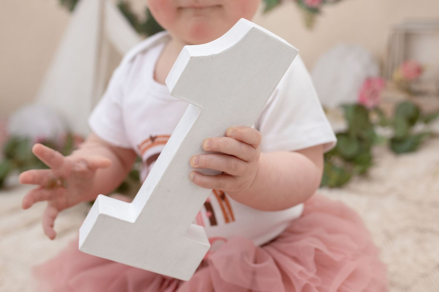 Close up of toddler holding large white number one decoration.