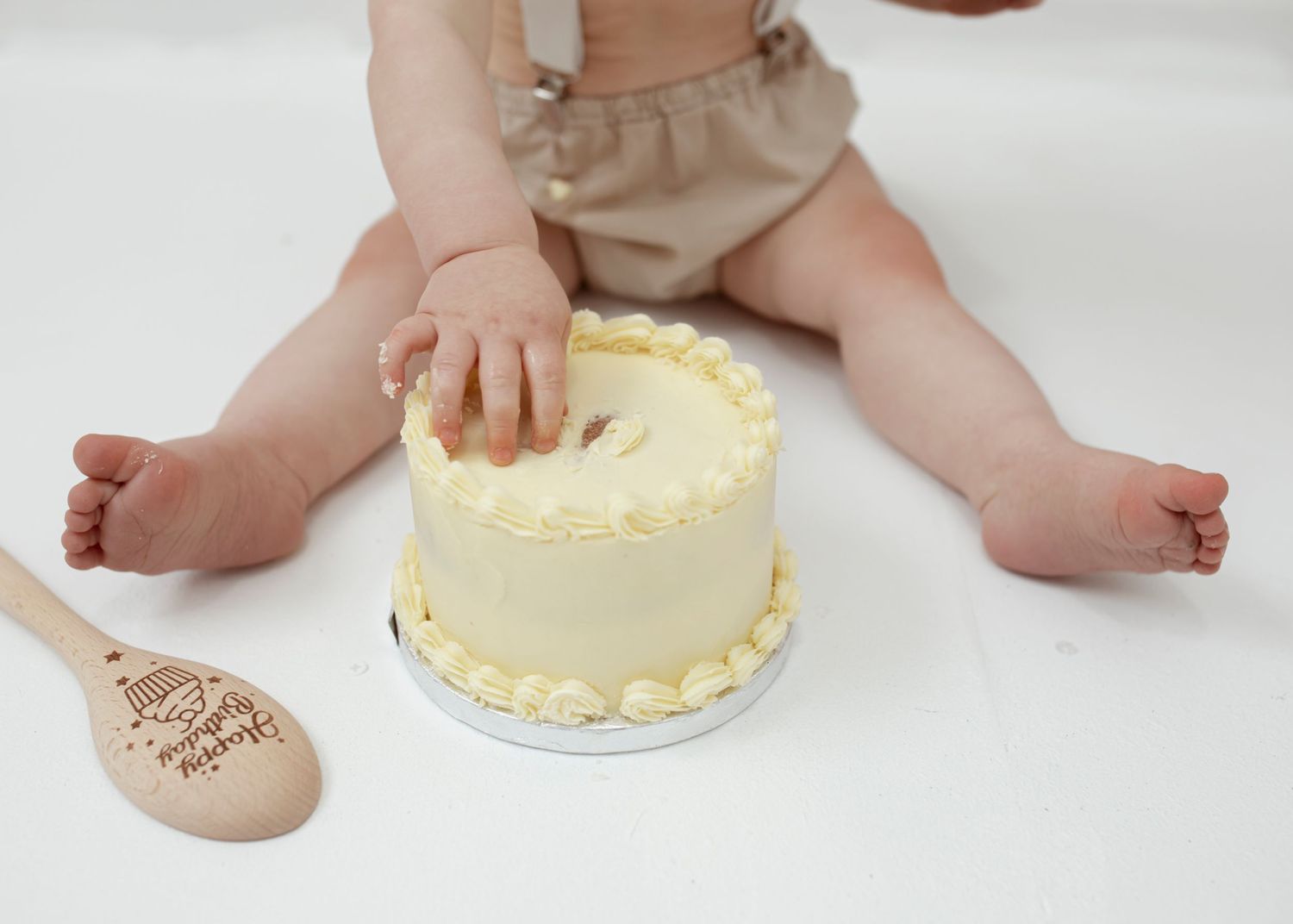Yellow birthday cake and wooden spoon on white floor with rustic decor.