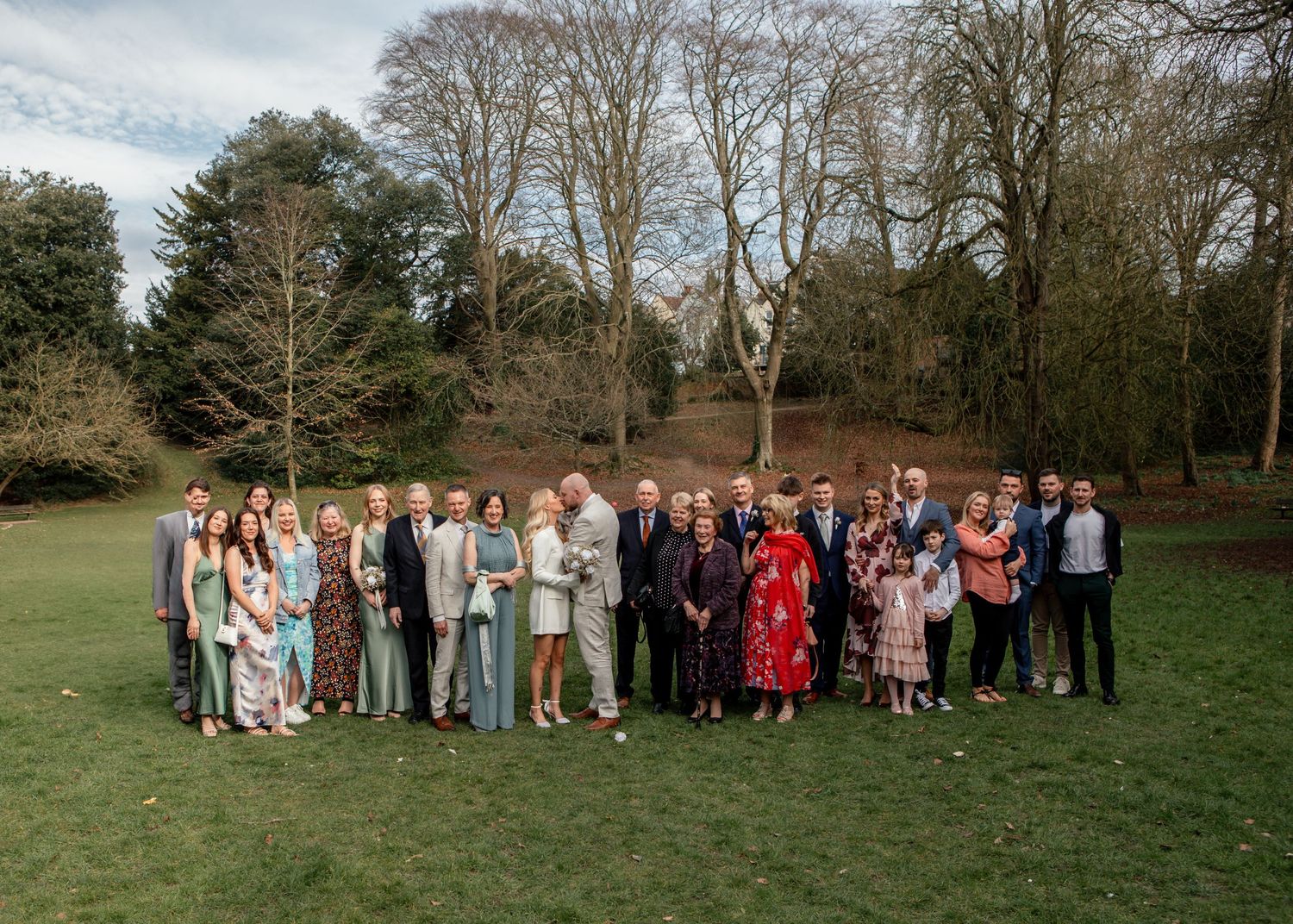 Large wedding group photo taken outdoors with trees in the background.