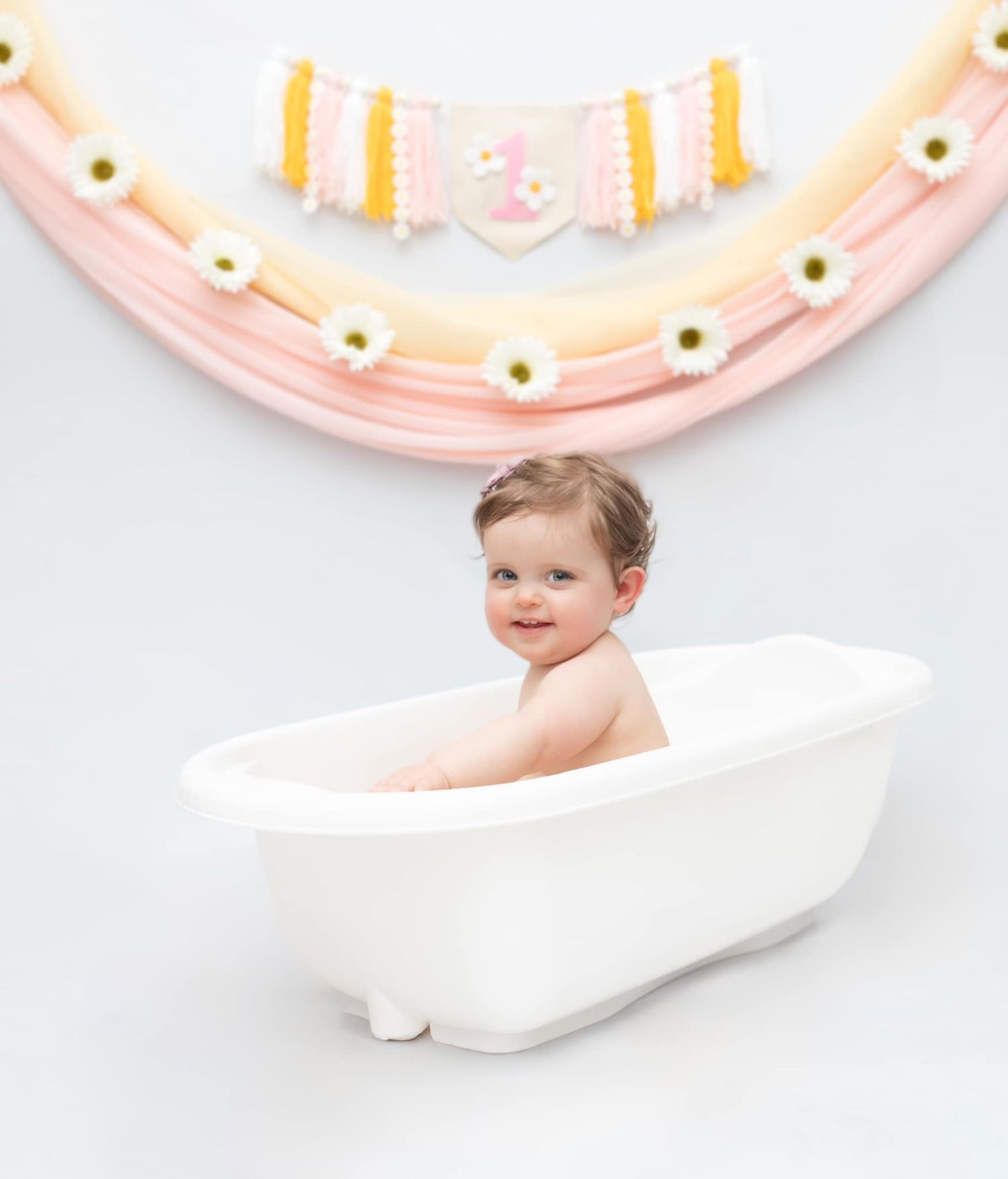 A pink birthday cake smash photo setup with decorative plates and banners in the background.