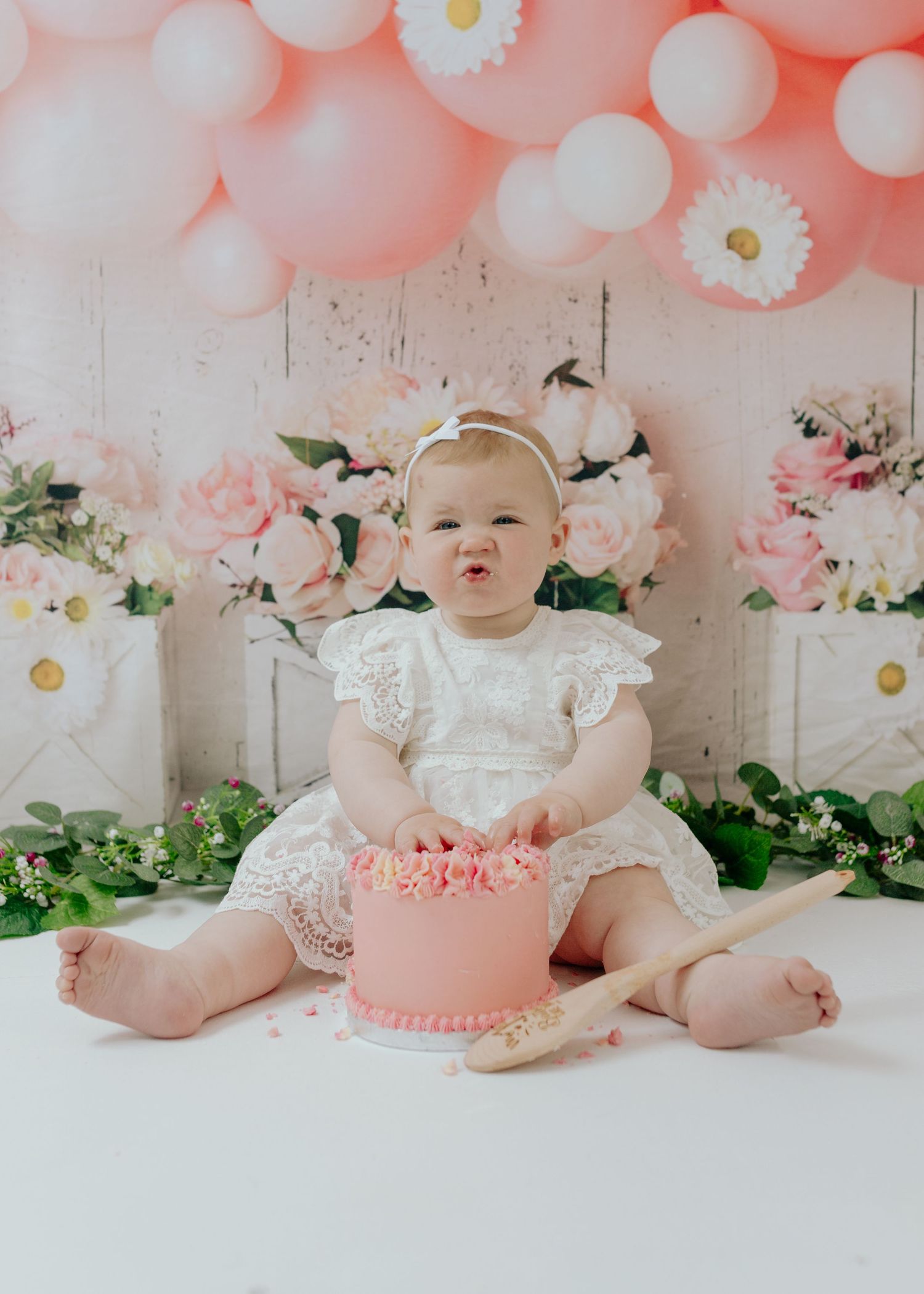 Baby sitting on white floor with pink balloon and floral decorations.