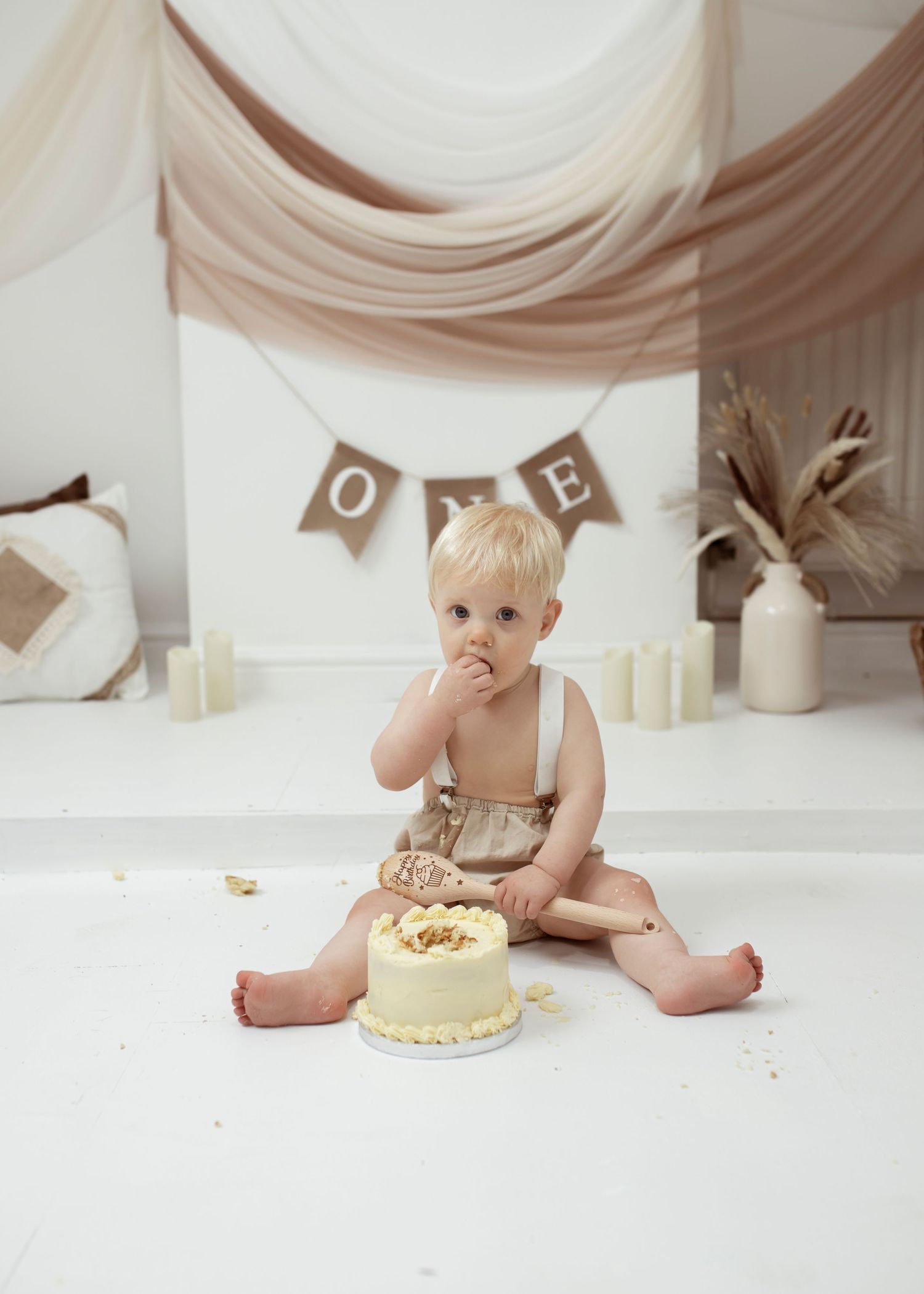 Neutral-toned cake smash photography setup with rustic banner and decorations.