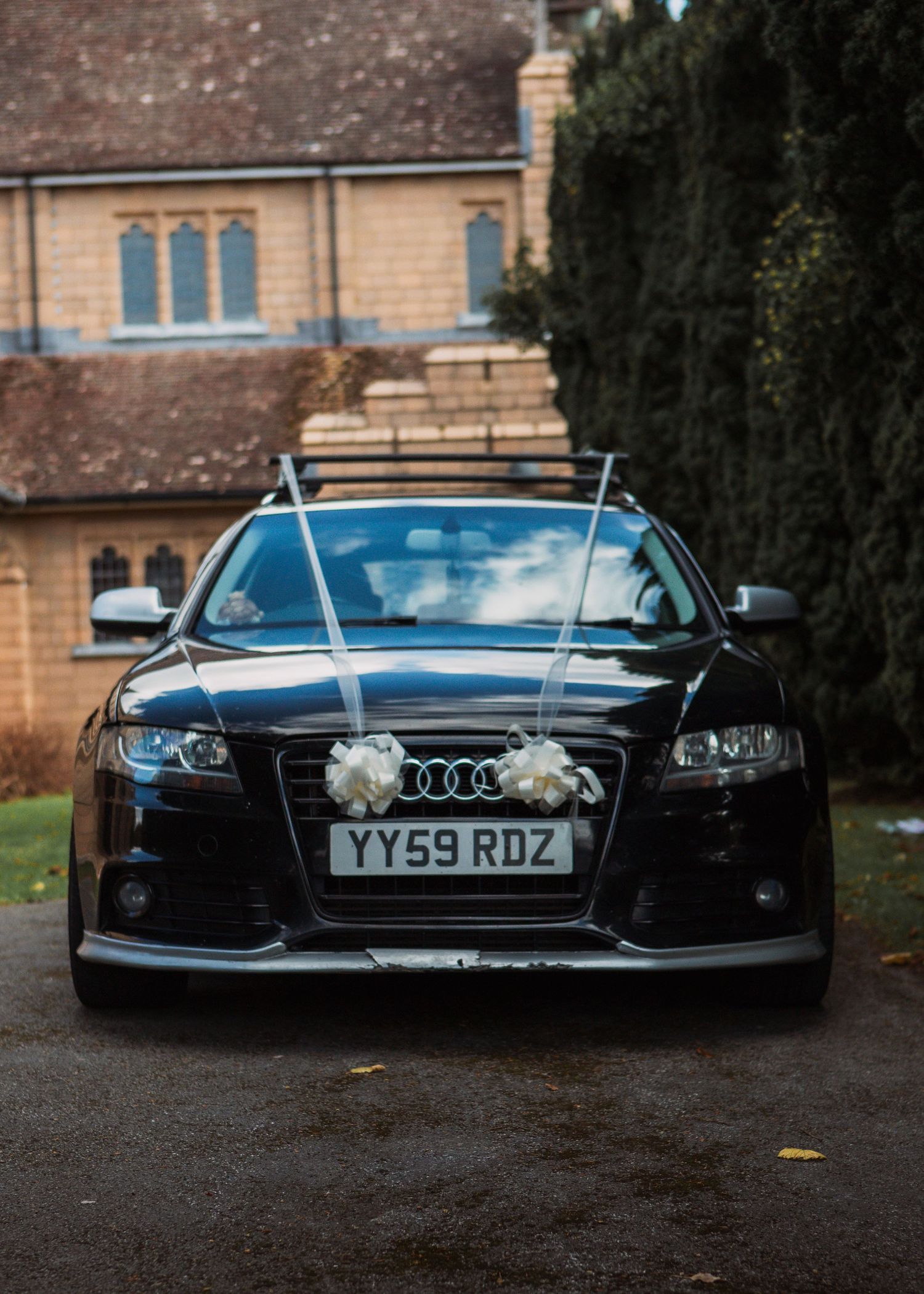 Row of black Audi cars decorated with wedding ribbons parked outside brick building.