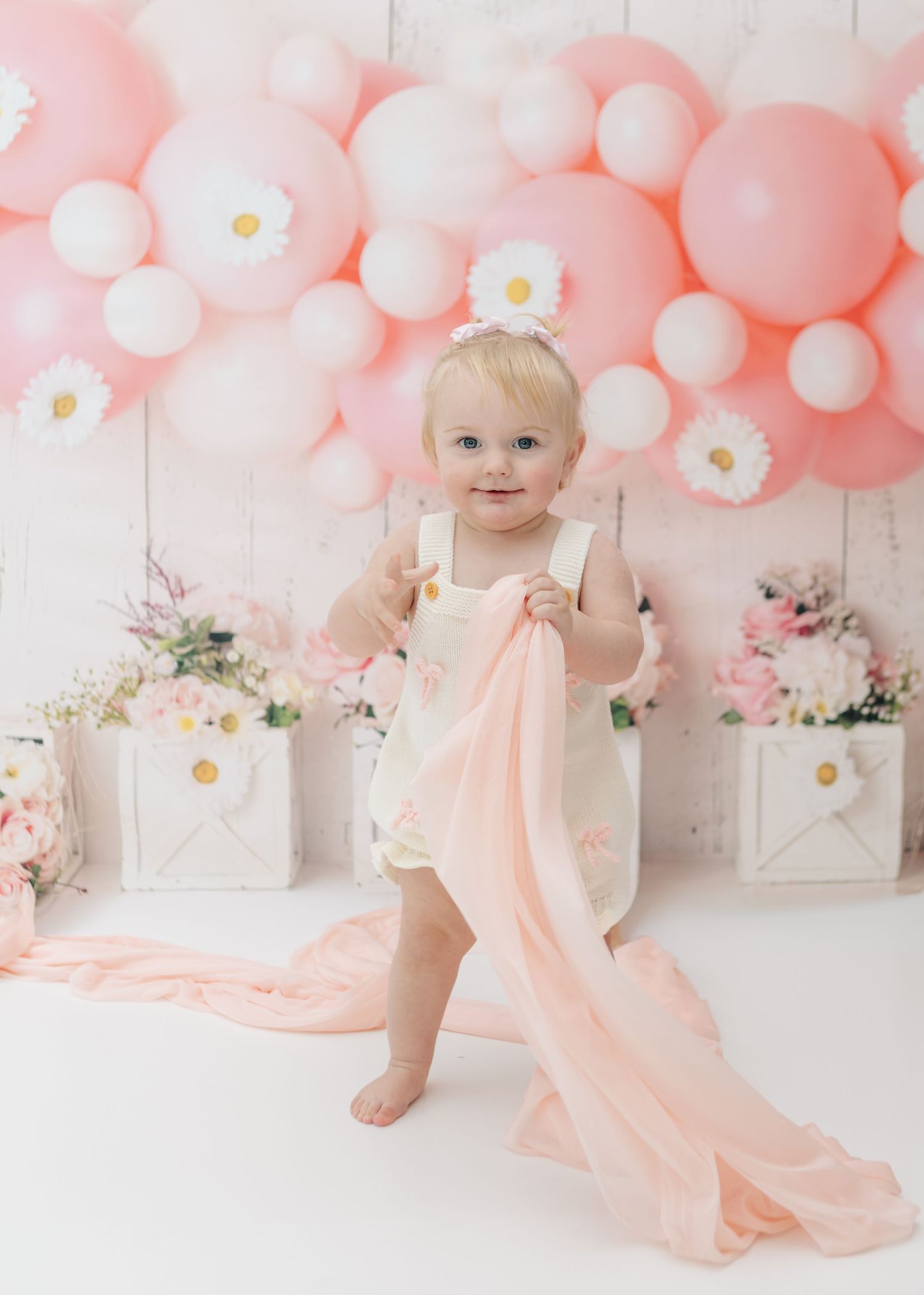 Pink and white balloon arch decorates backdrop for baby photo with daisy accents.