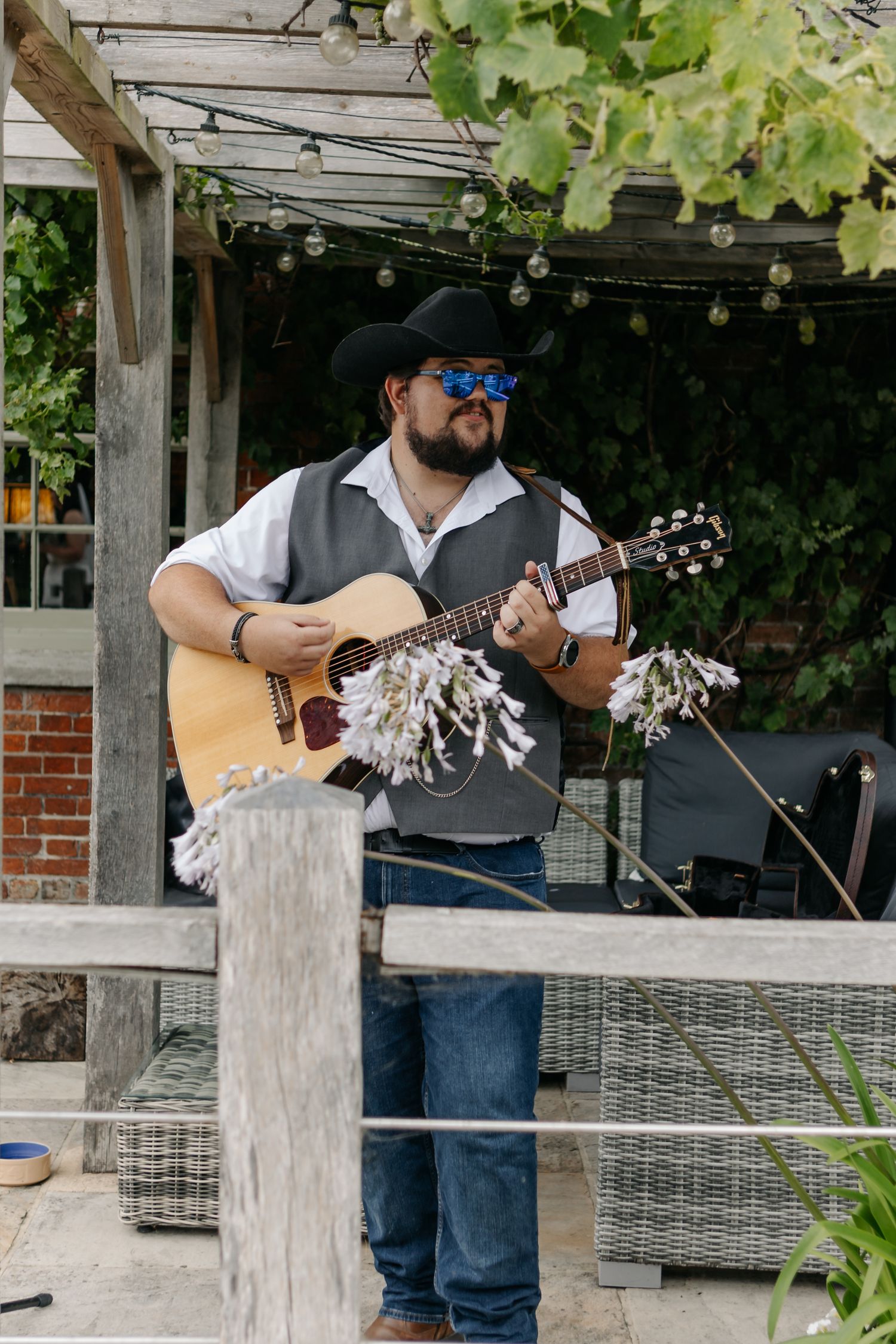 Musicians performing with acoustic guitars under a covered outdoor patio.