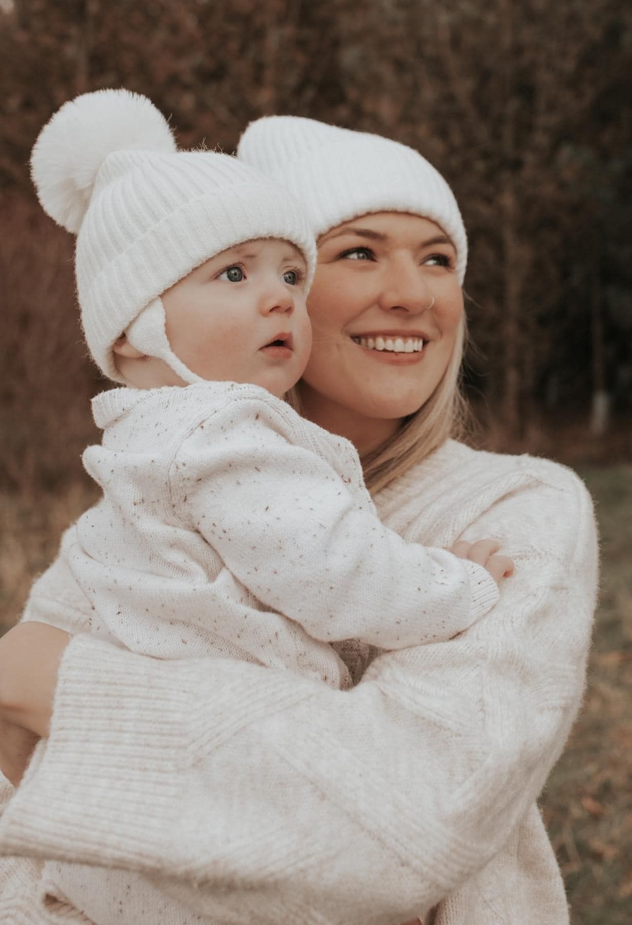 Sweet candid moment captured in cream colored winter outfits against a natural backdrop.