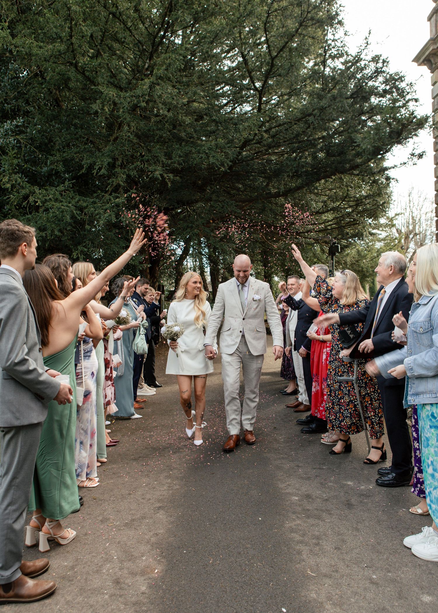 Wedding couple walking through crowd throwing confetti on path.