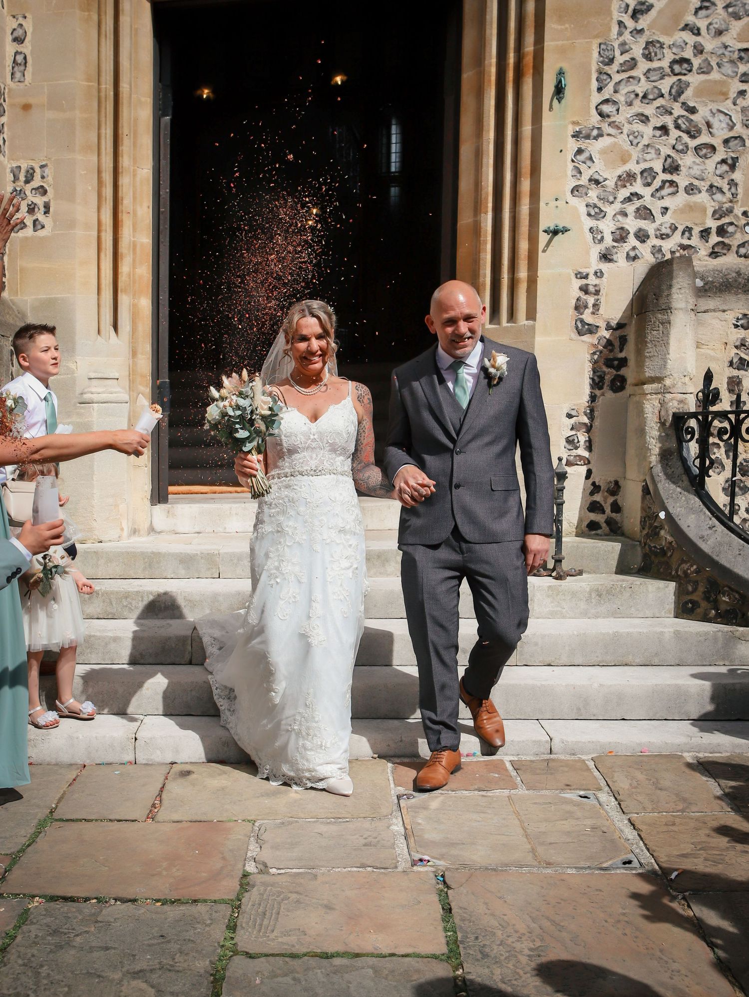 Wedding couple celebrating with confetti toss on stone church steps.