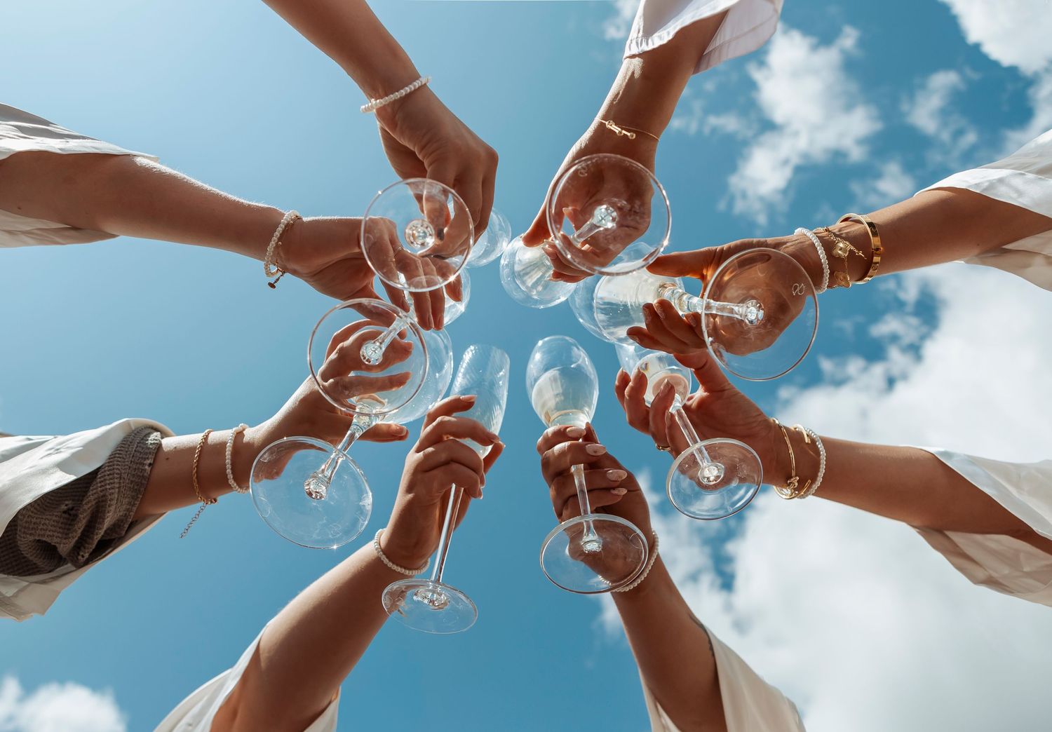 Aerial view of hands holding champagne glasses in a circle against a blue sky.