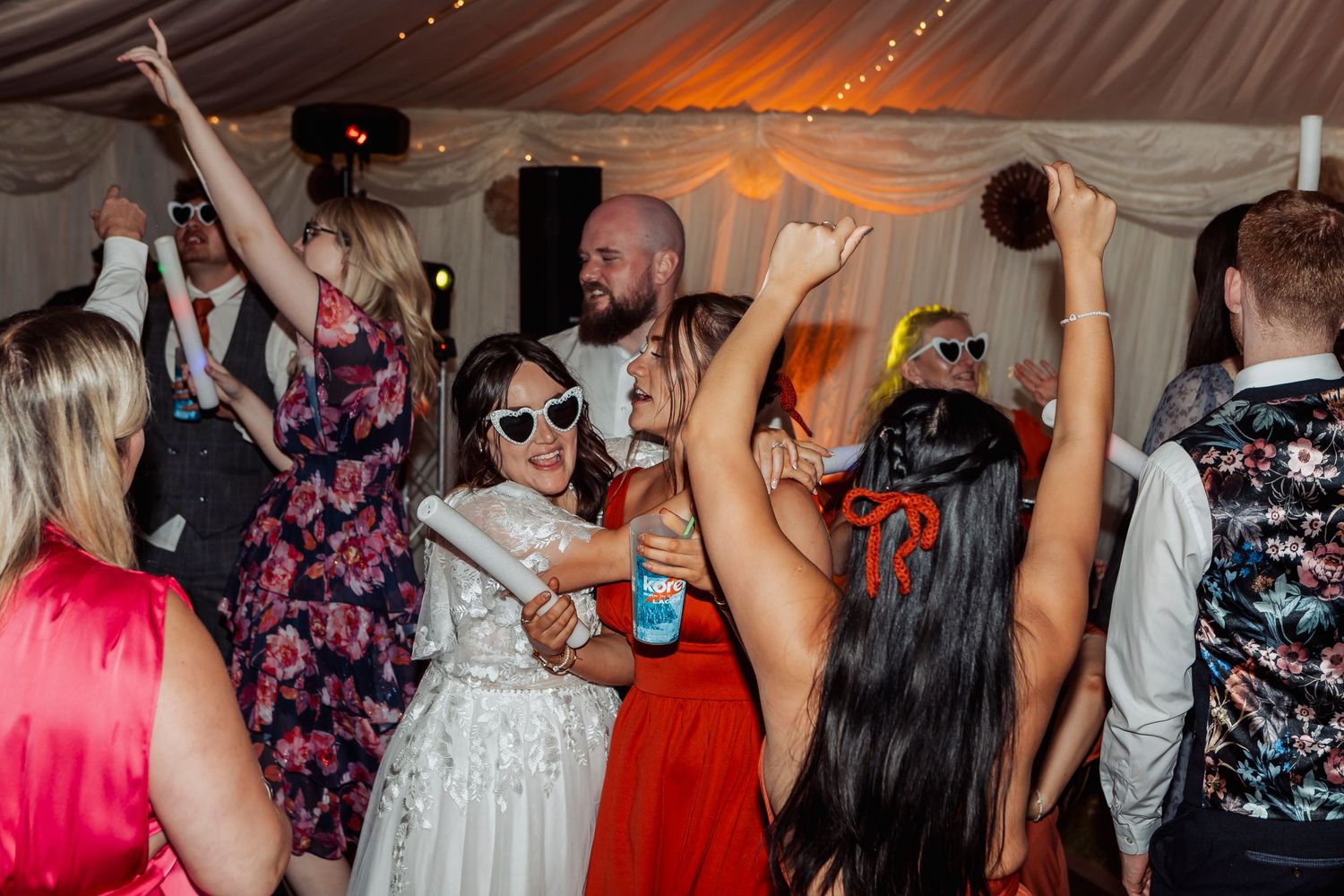 Lively dance floor scene with guests celebrating at a wedding reception under decorative lighting.