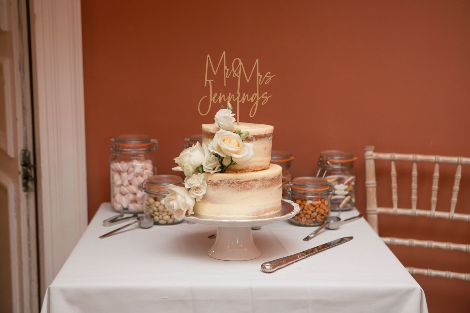 Elegant wedding cake display on white tablecloth with rustic decor.